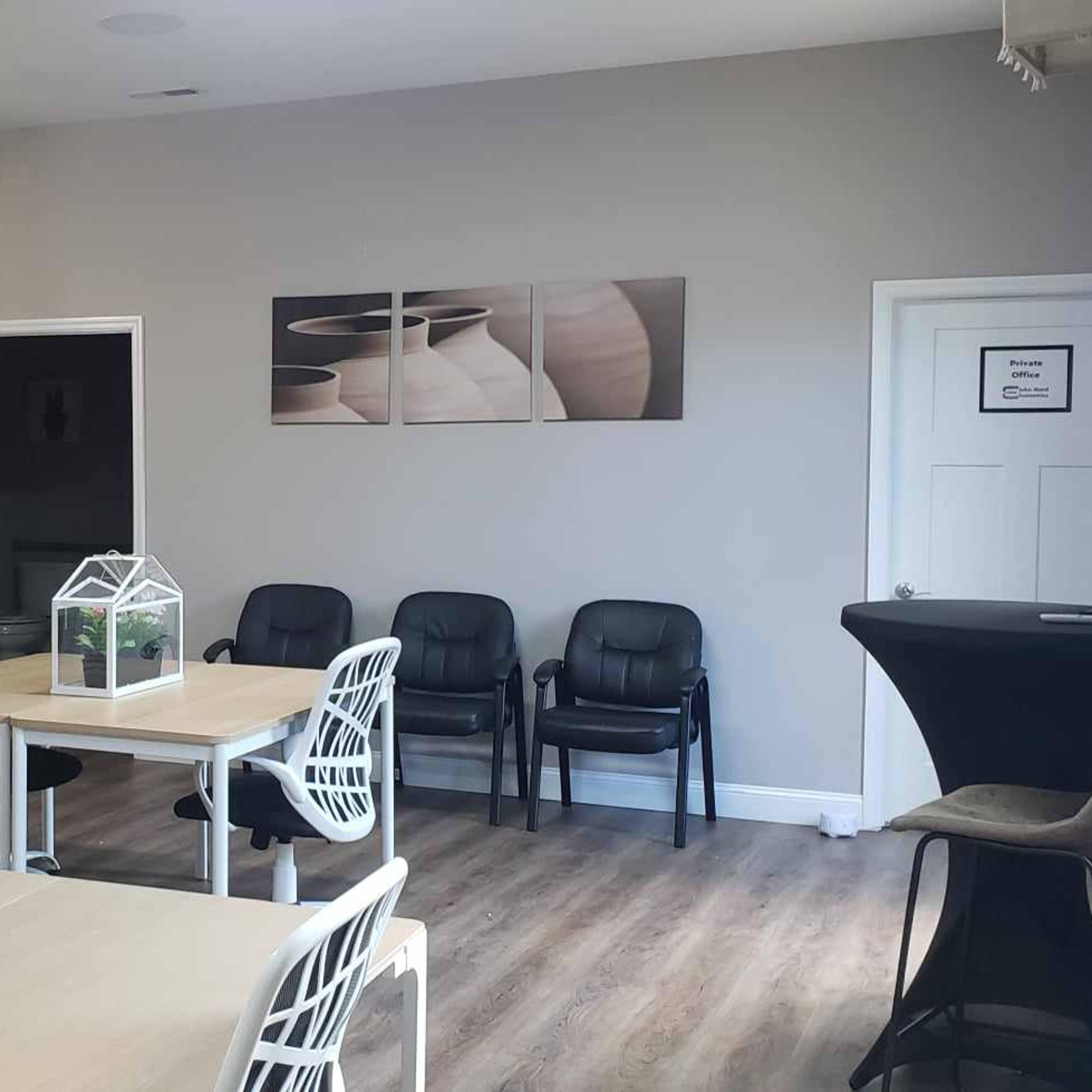 A modern, open interior space with wooden flooring, tables, chairs, and a kitchenette area in the background.