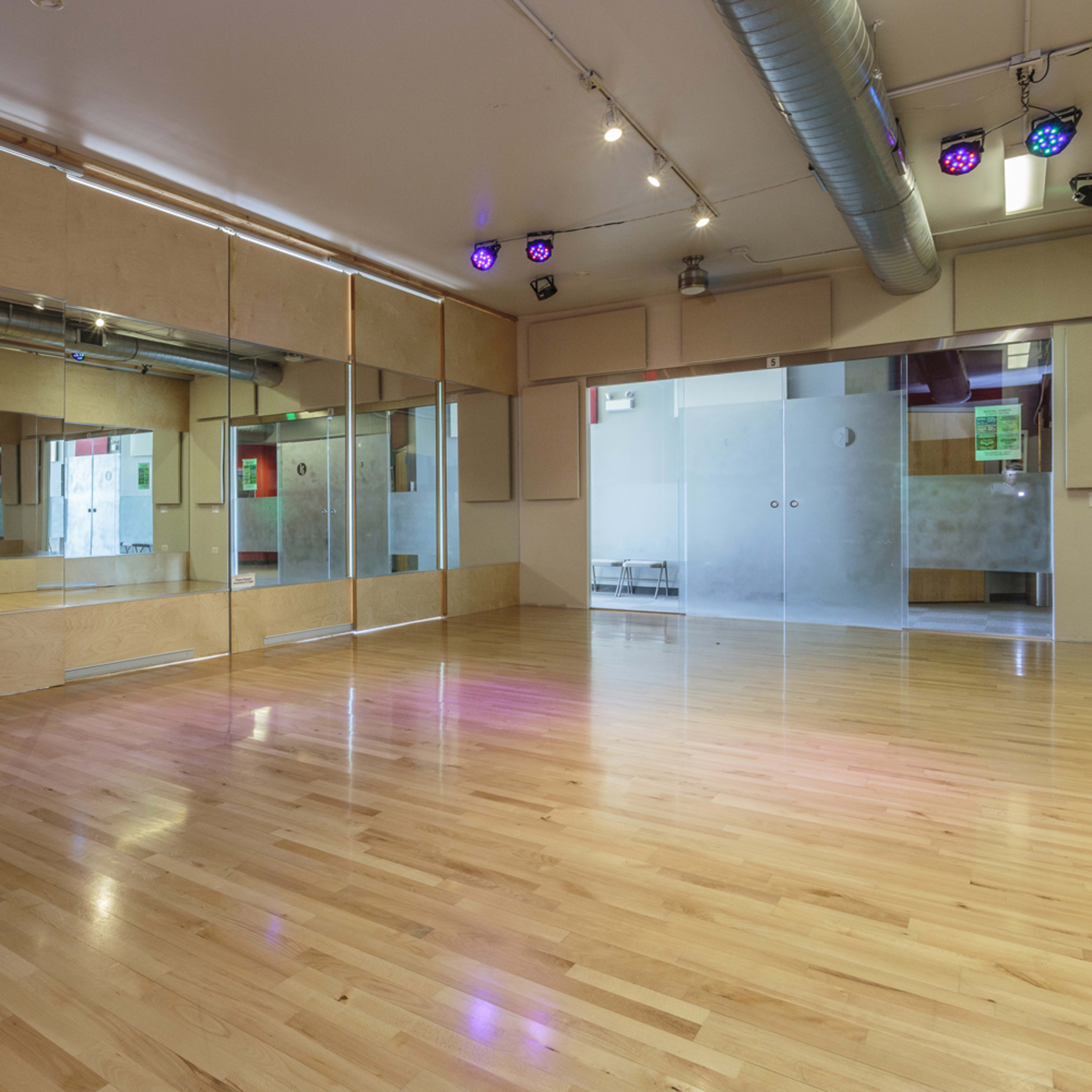 An empty dance studio featuring wooden flooring, mirrored walls, and various lighting fixtures.