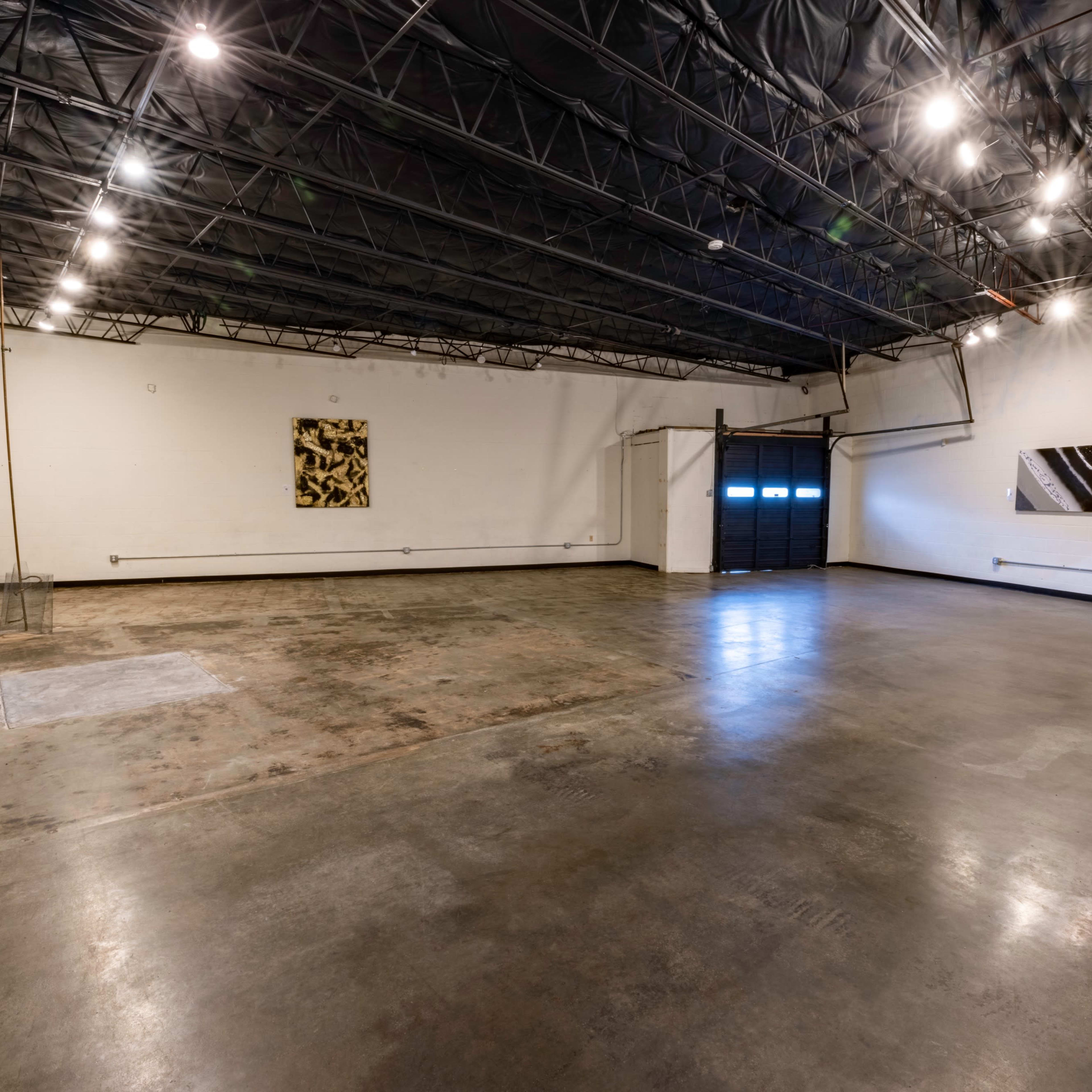An empty industrial space with a polished concrete floor, dim lighting, and two abstract art pieces on the walls.