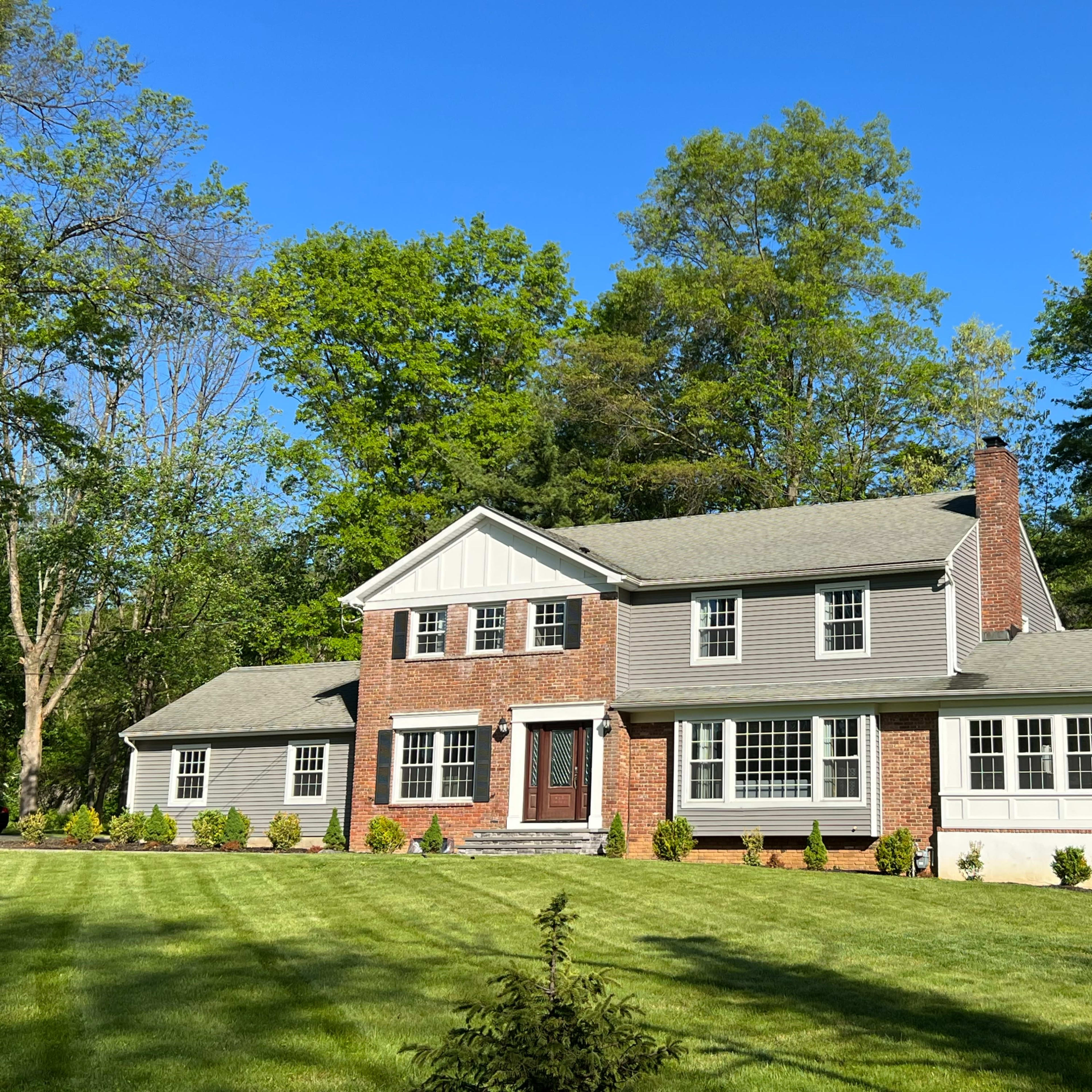 A two-story house with a combination of brick and siding sits on a well-maintained lawn surrounded by trees.