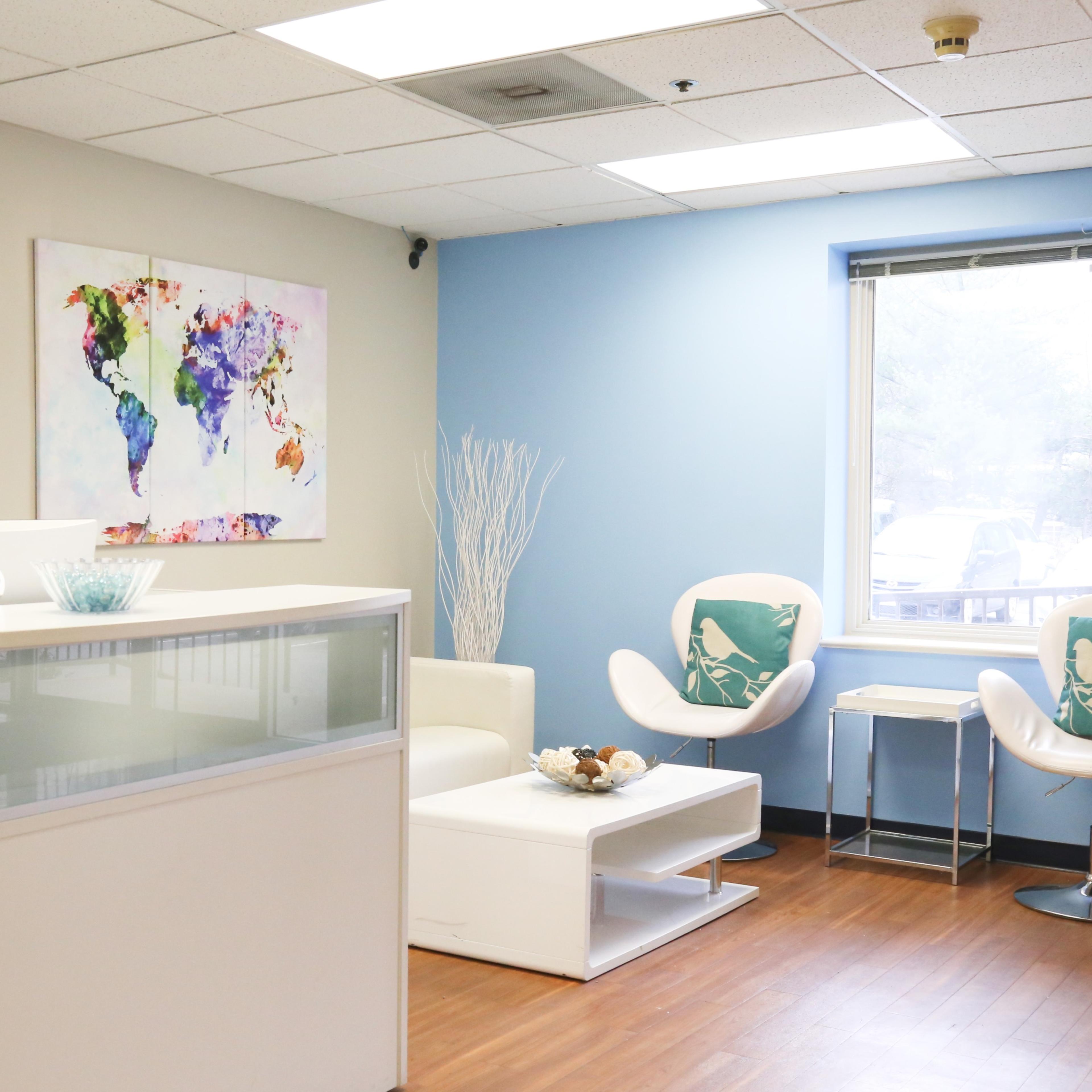 A modern office reception area with a white front desk, two white chairs with decorative cushions, and a colorful world map on the wall.