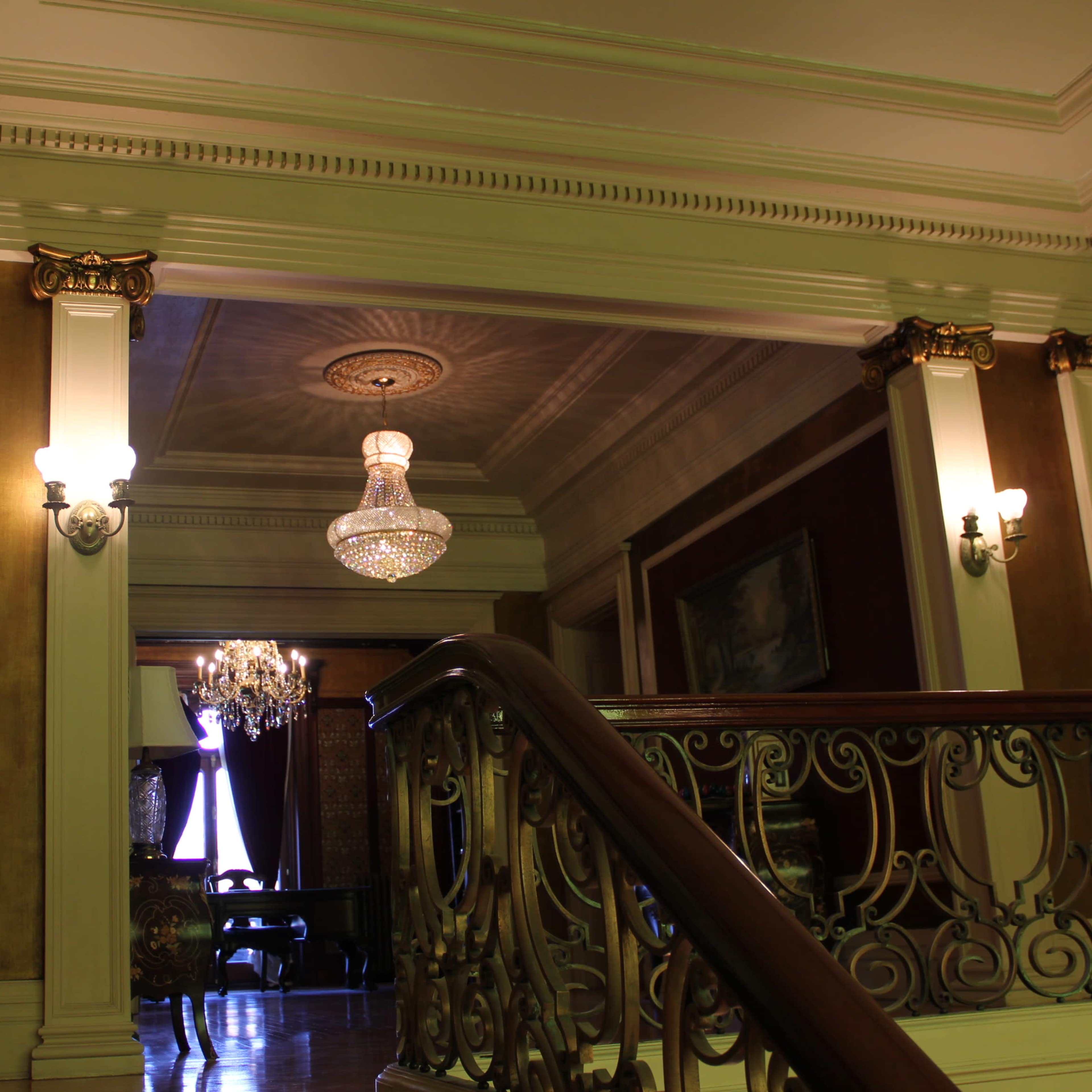 An ornate hallway in a historical building, featuring a chandelier and a curved wooden staircase.