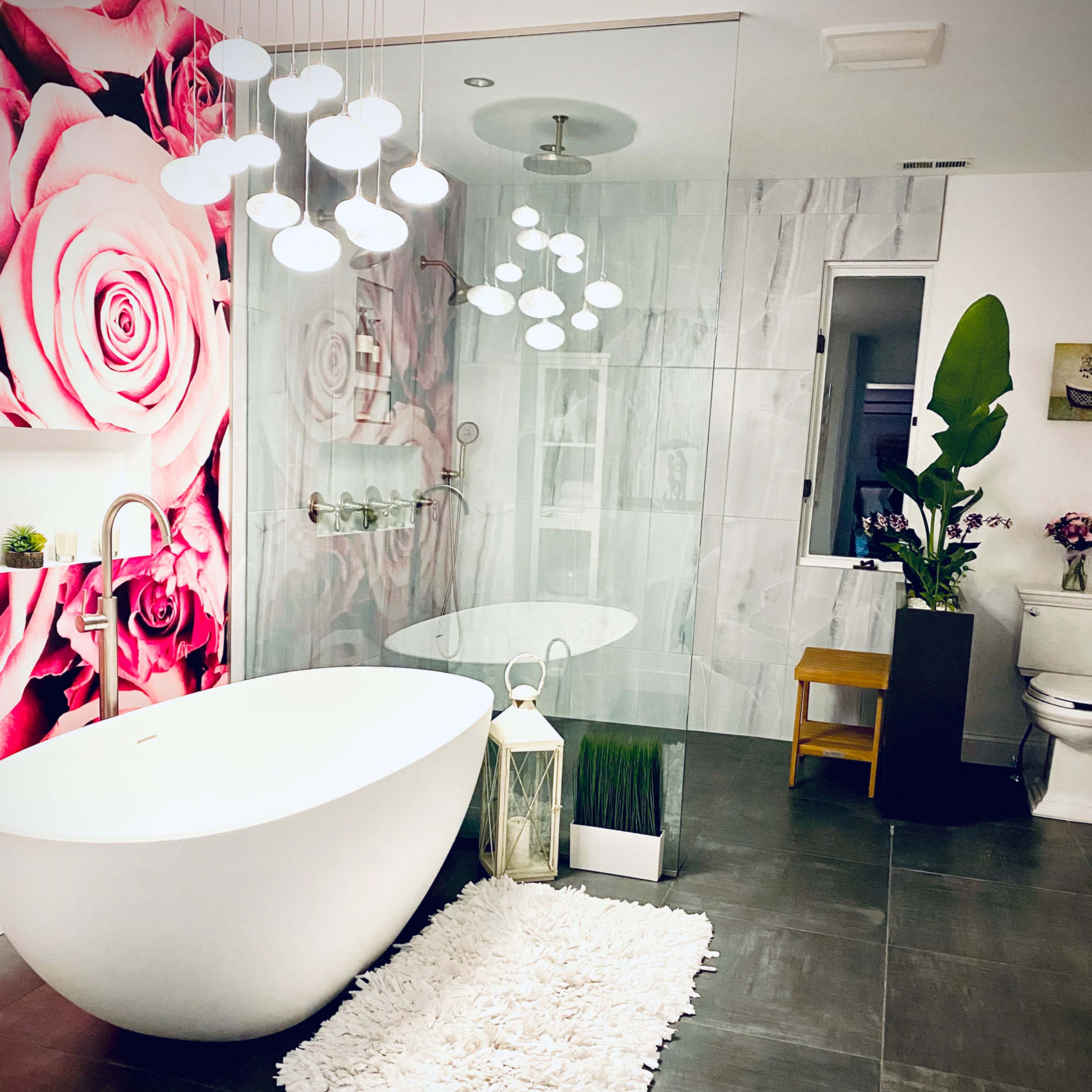 A modern bathroom featuring a freestanding white bathtub, a glass shower enclosure, floral wallpaper, and decorative plants.