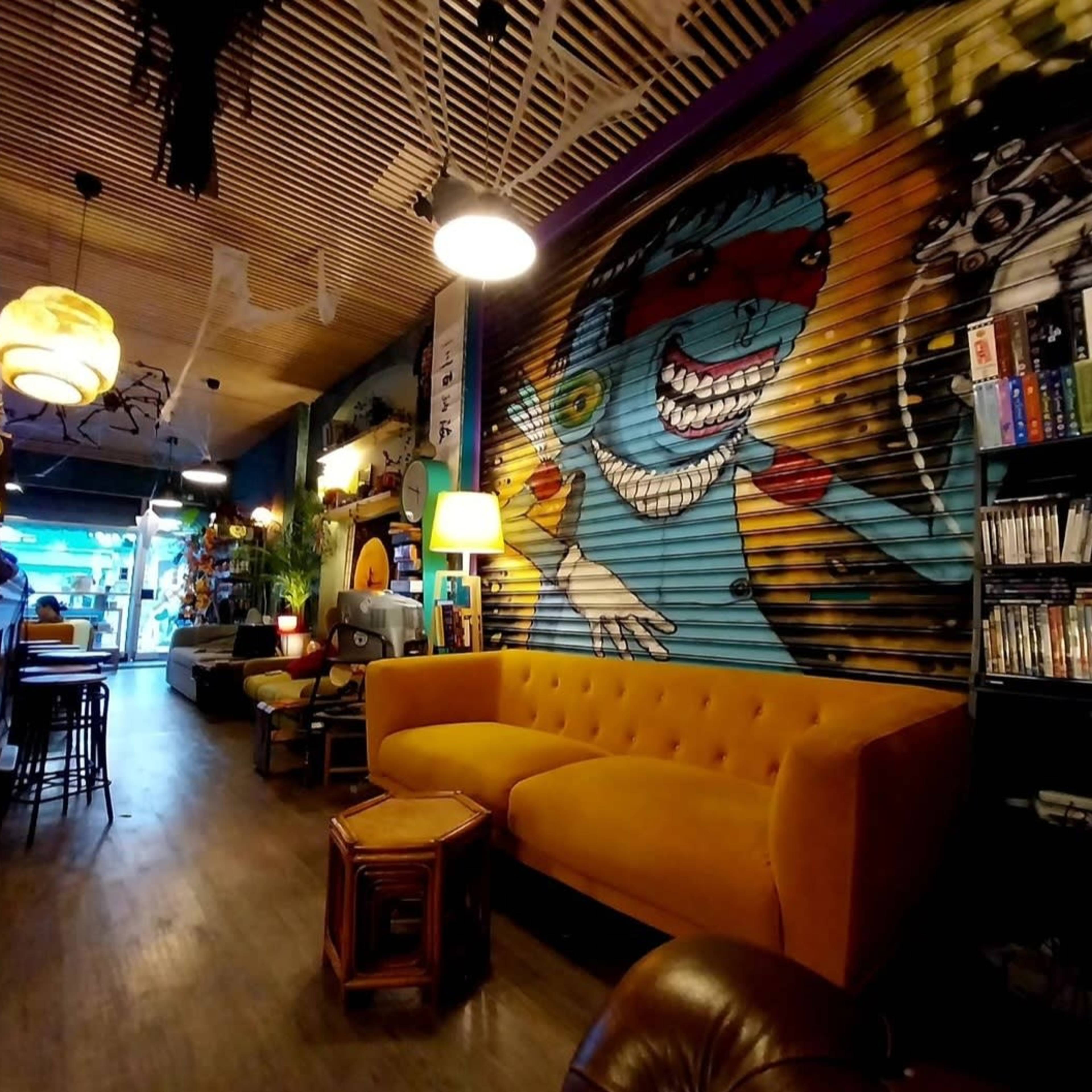 The scene features a cozy café with a vibrant mural, yellow tufted sofa, and warm lighting.