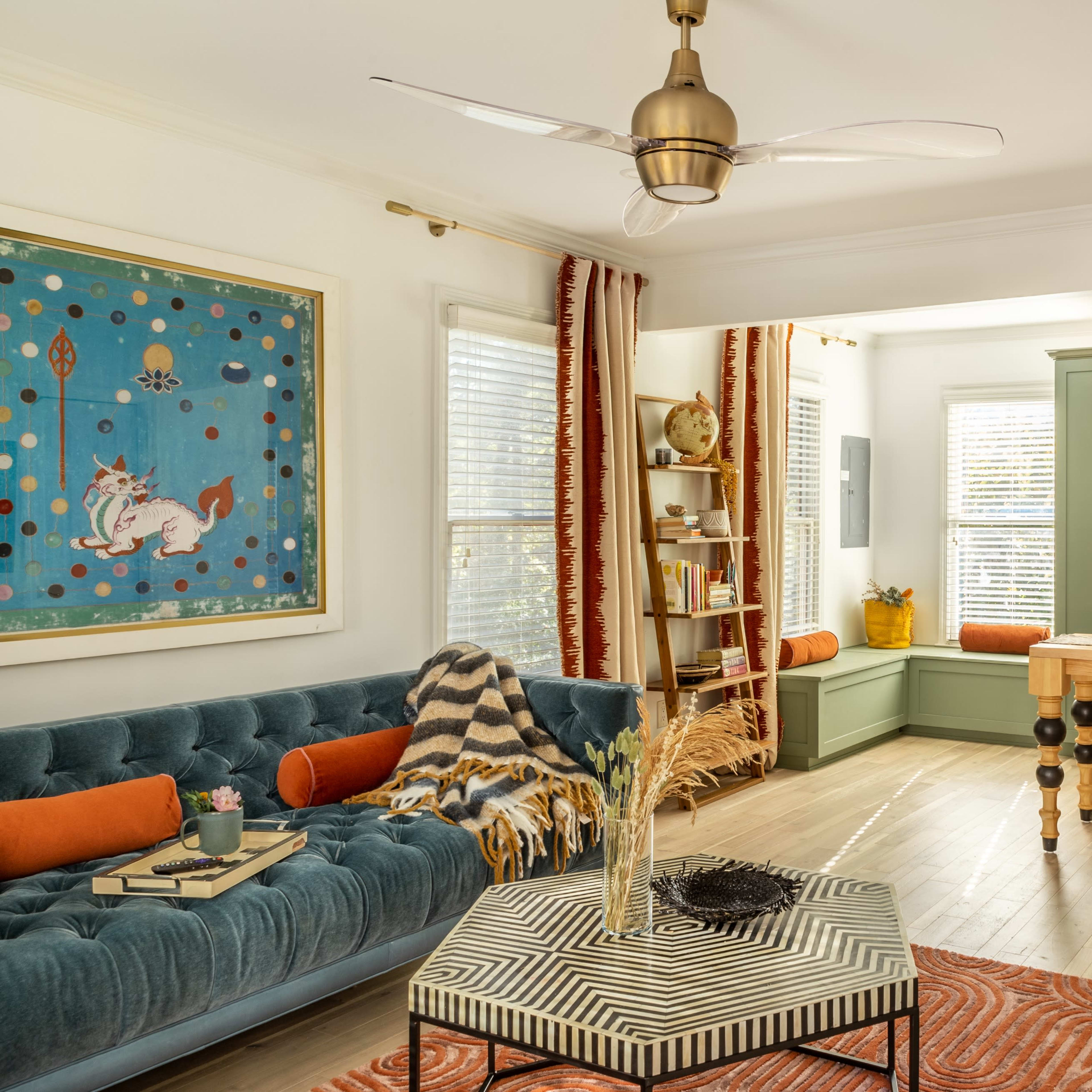 A contemporary living space featuring a blue velvet sofa, an adjoining kitchen with green cabinetry, and large windows that allow natural light to fill the room.