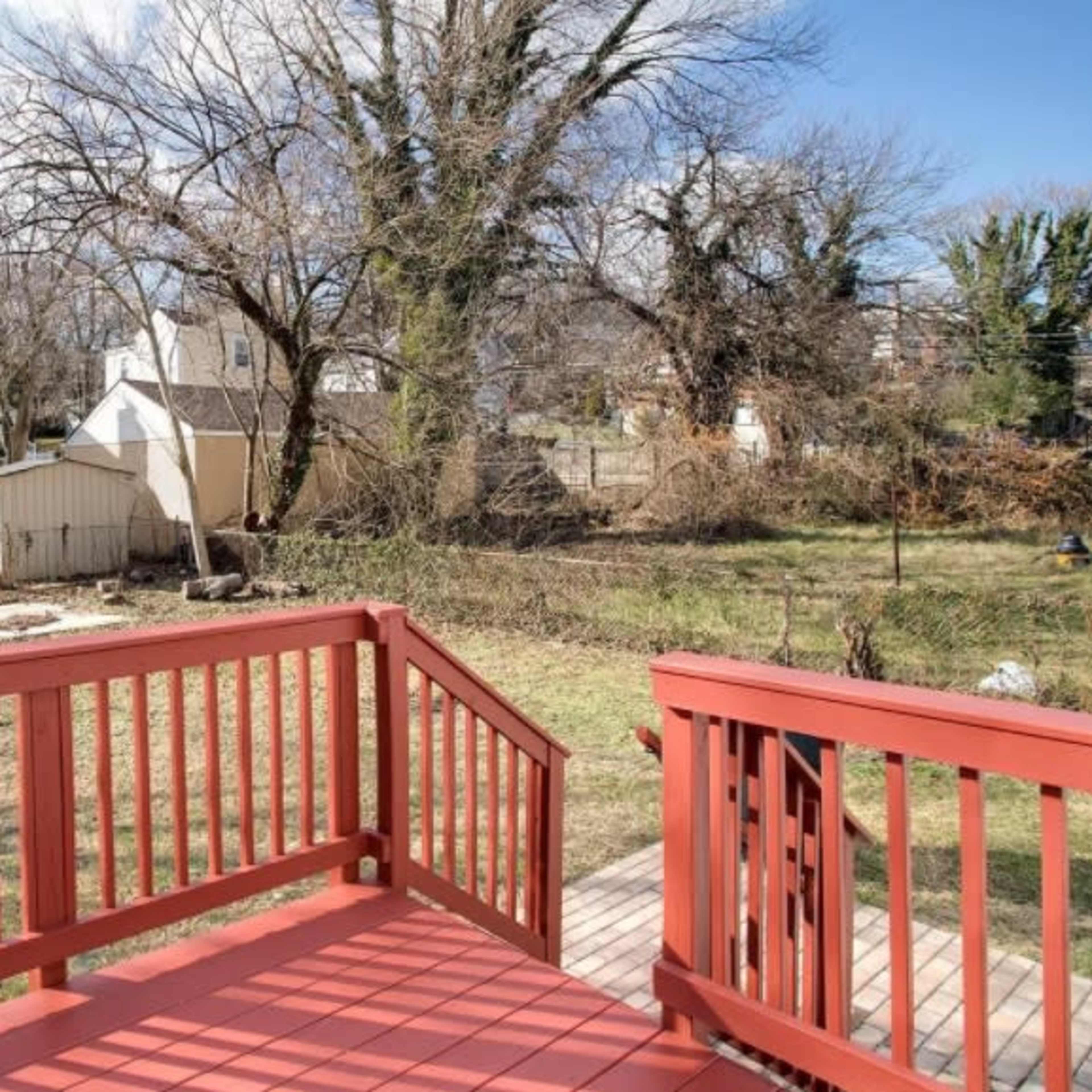 A red wooden deck overlooking a grassy yard with several homes and bare trees in the background.