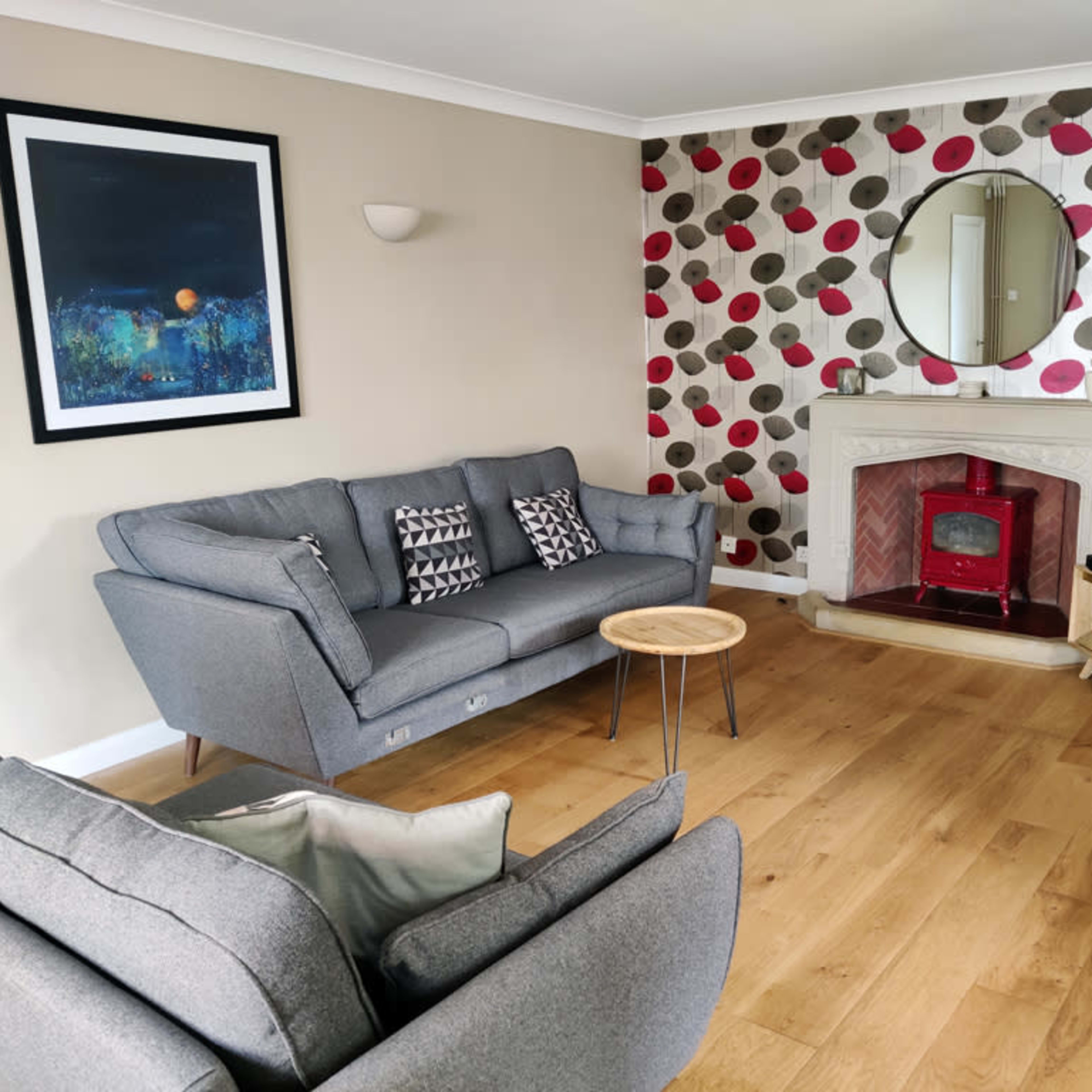 The living room features a gray sofa set, a round mirror above a fireplace, and a television mounted on a wooden cabinet against a wall decorated with patterned circles.