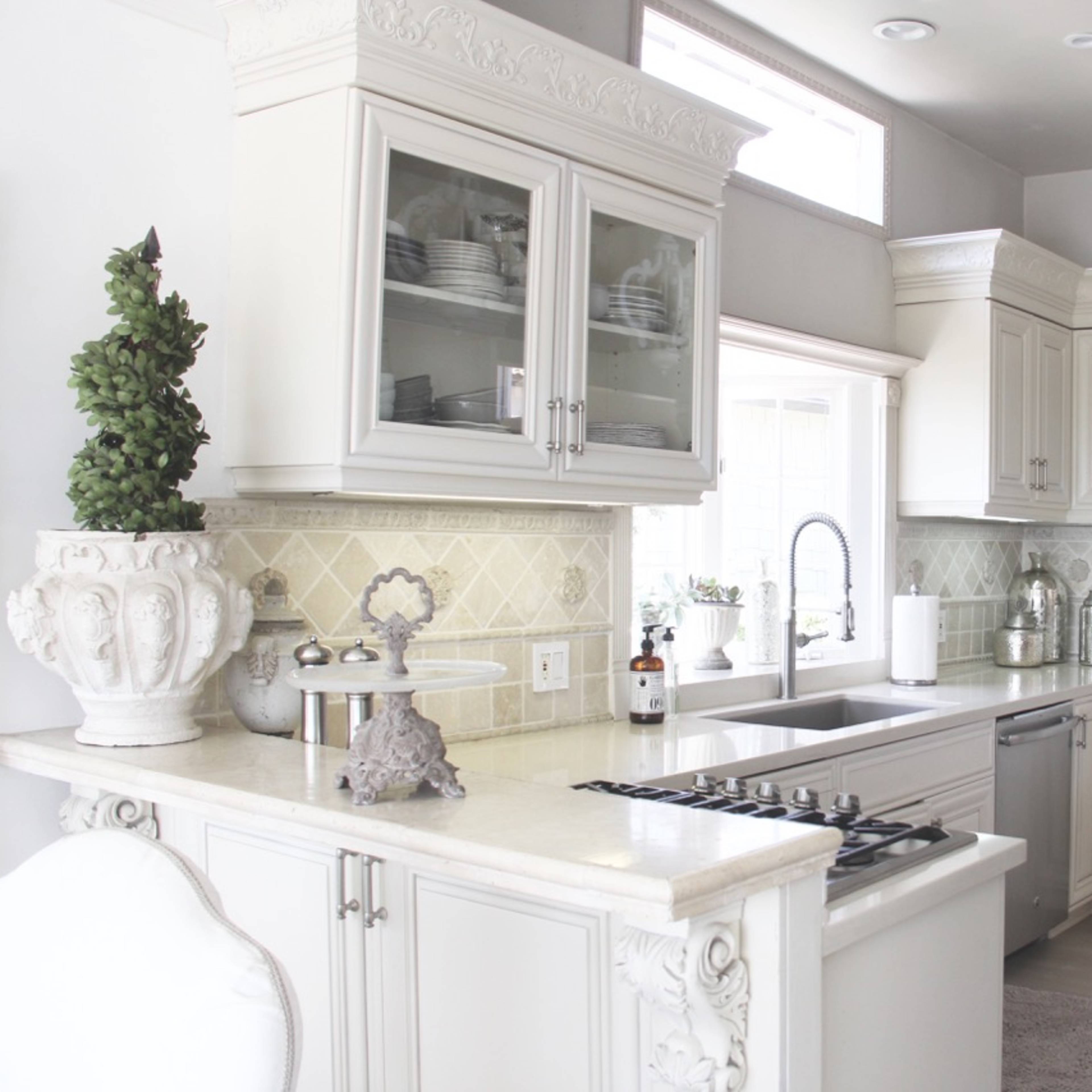 A bright, modern kitchen with white cabinetry, a stone countertop, and a chandelier.