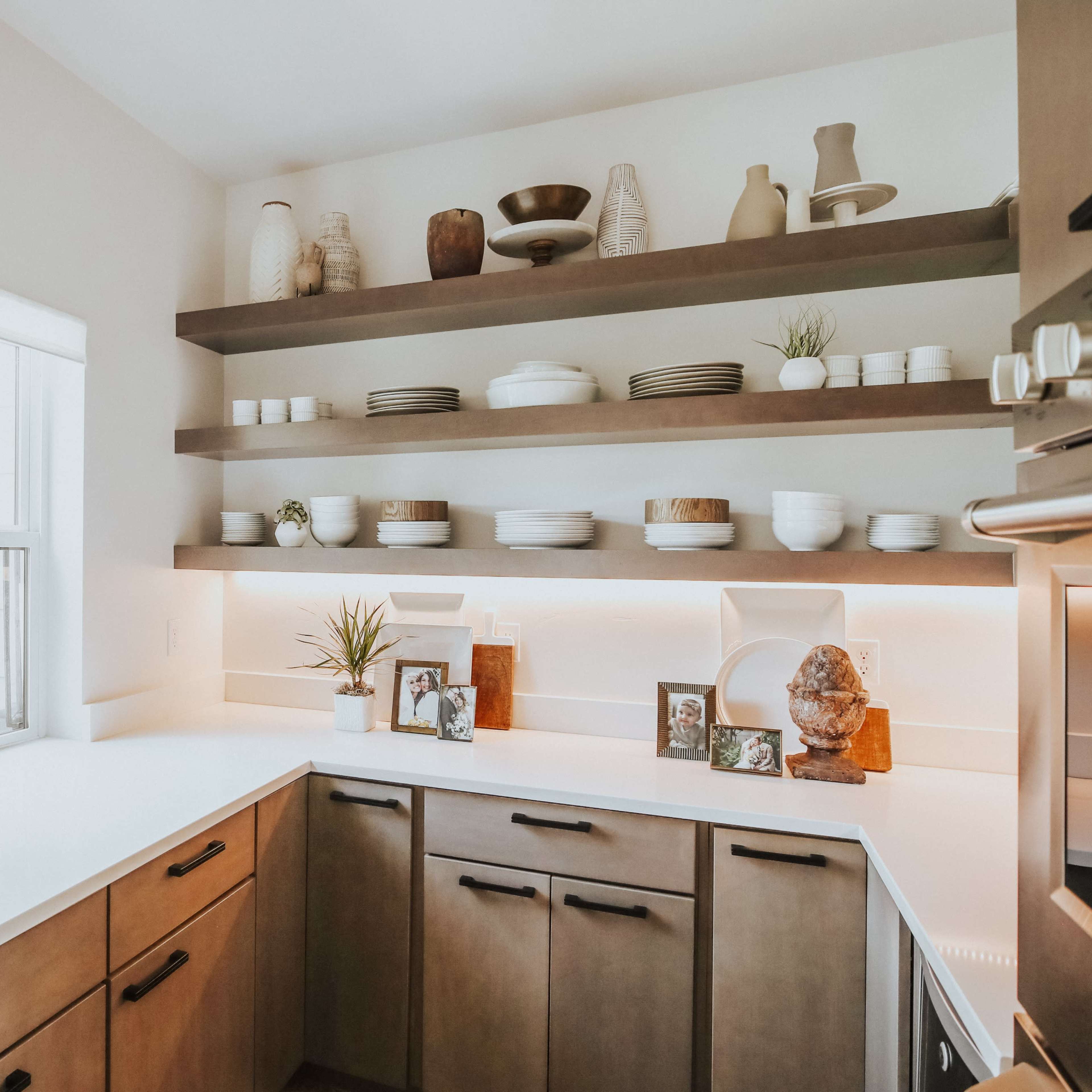A modern kitchen features white walls, wooden cabinets, and open shelving displaying various dishes and decorative items.