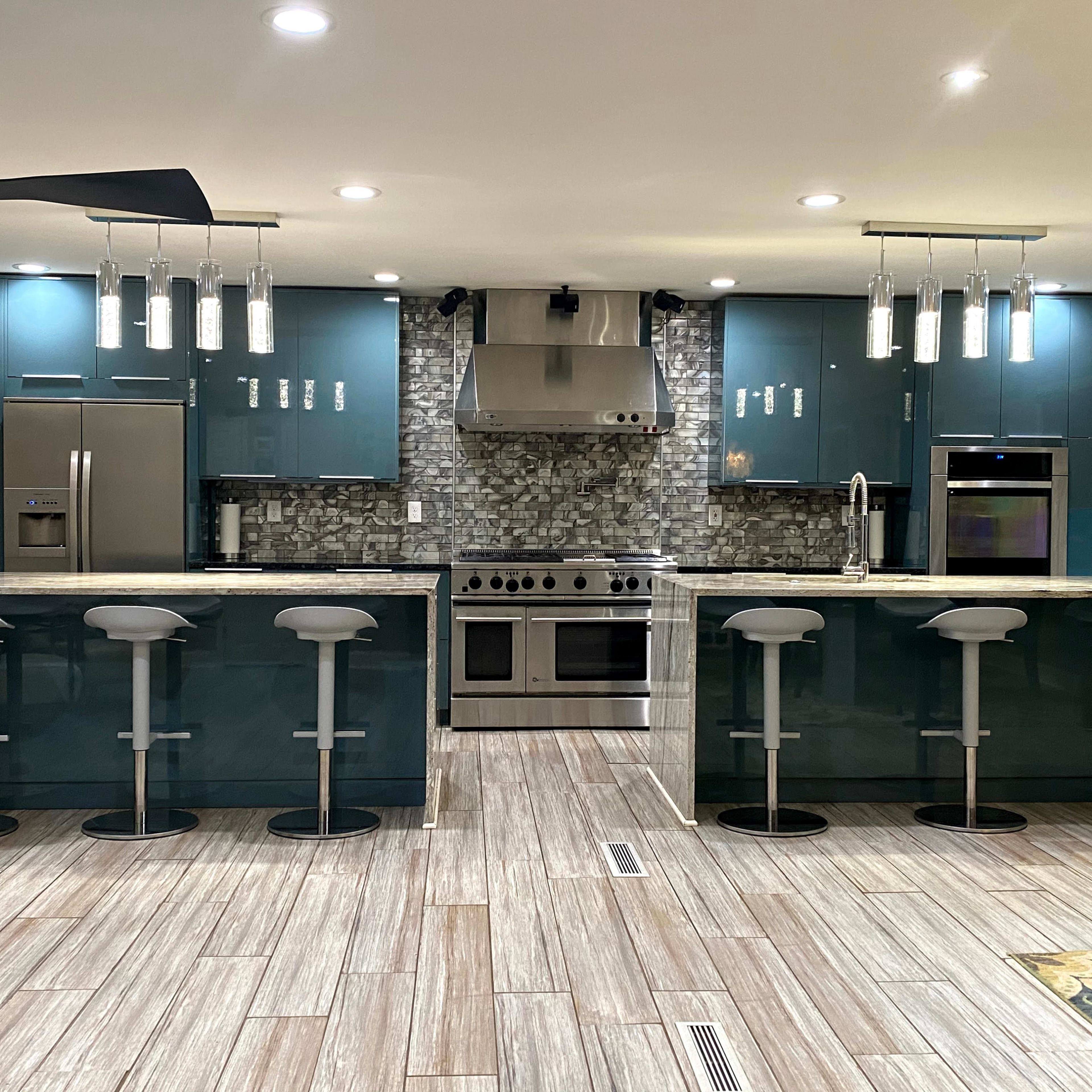 A modern kitchen with teal cabinets, a stainless steel stove, and a large island with four white bar stools.
