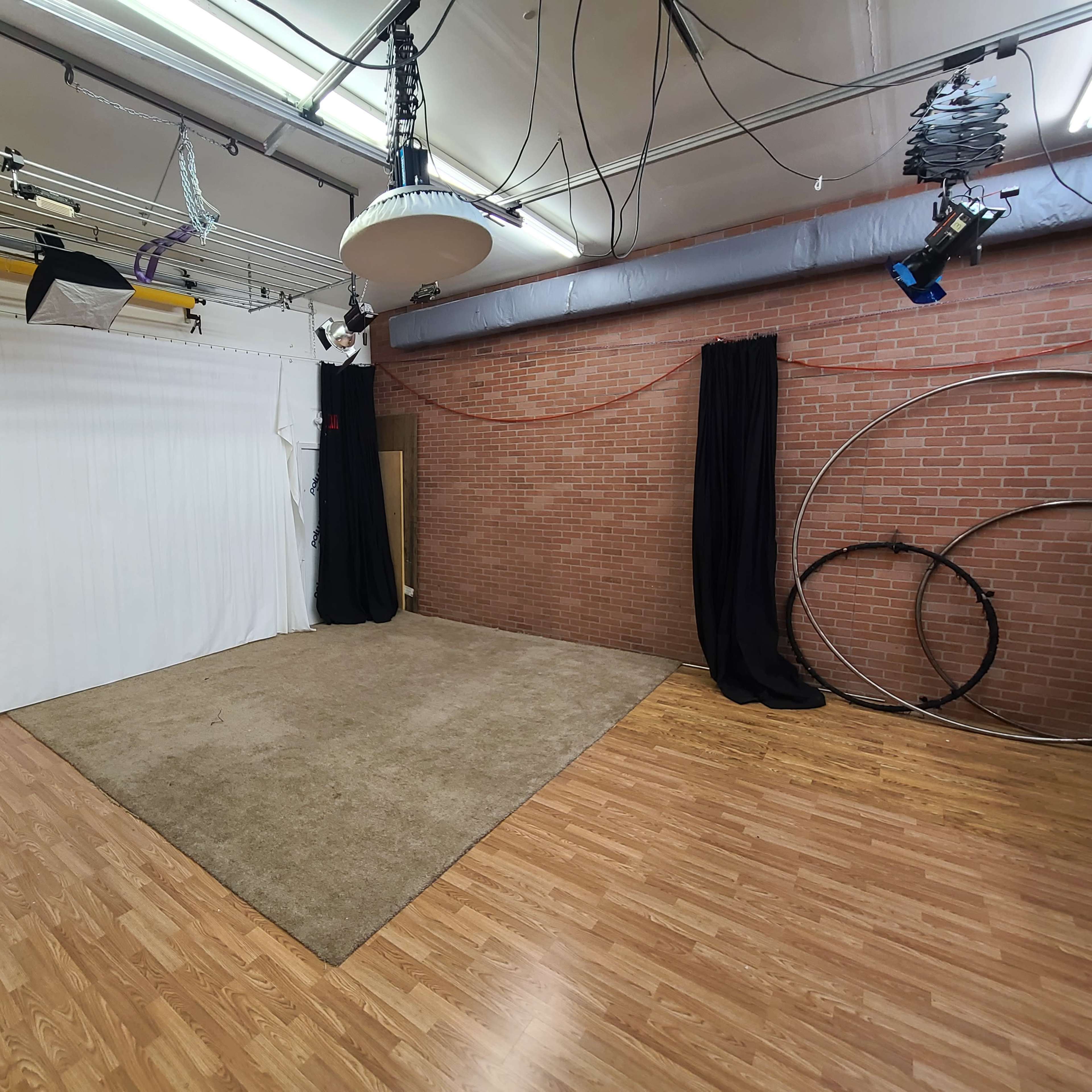 A spacious photography studio featuring a white backdrop, a carpeted area, and various lighting equipment hanging from the ceiling.