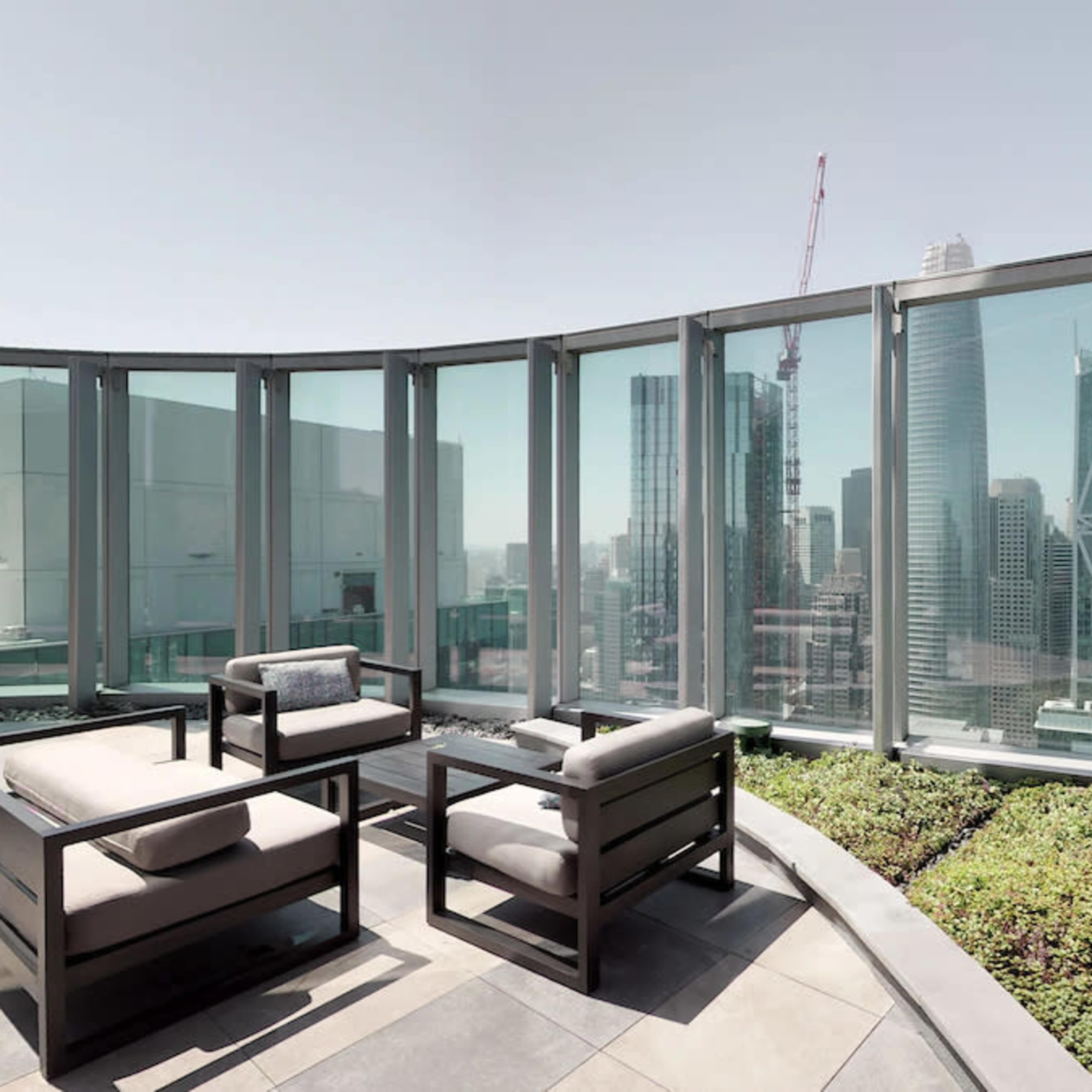 A rooftop terrace features modern furniture and panoramic views of city skyscrapers surrounded by glass partitions.