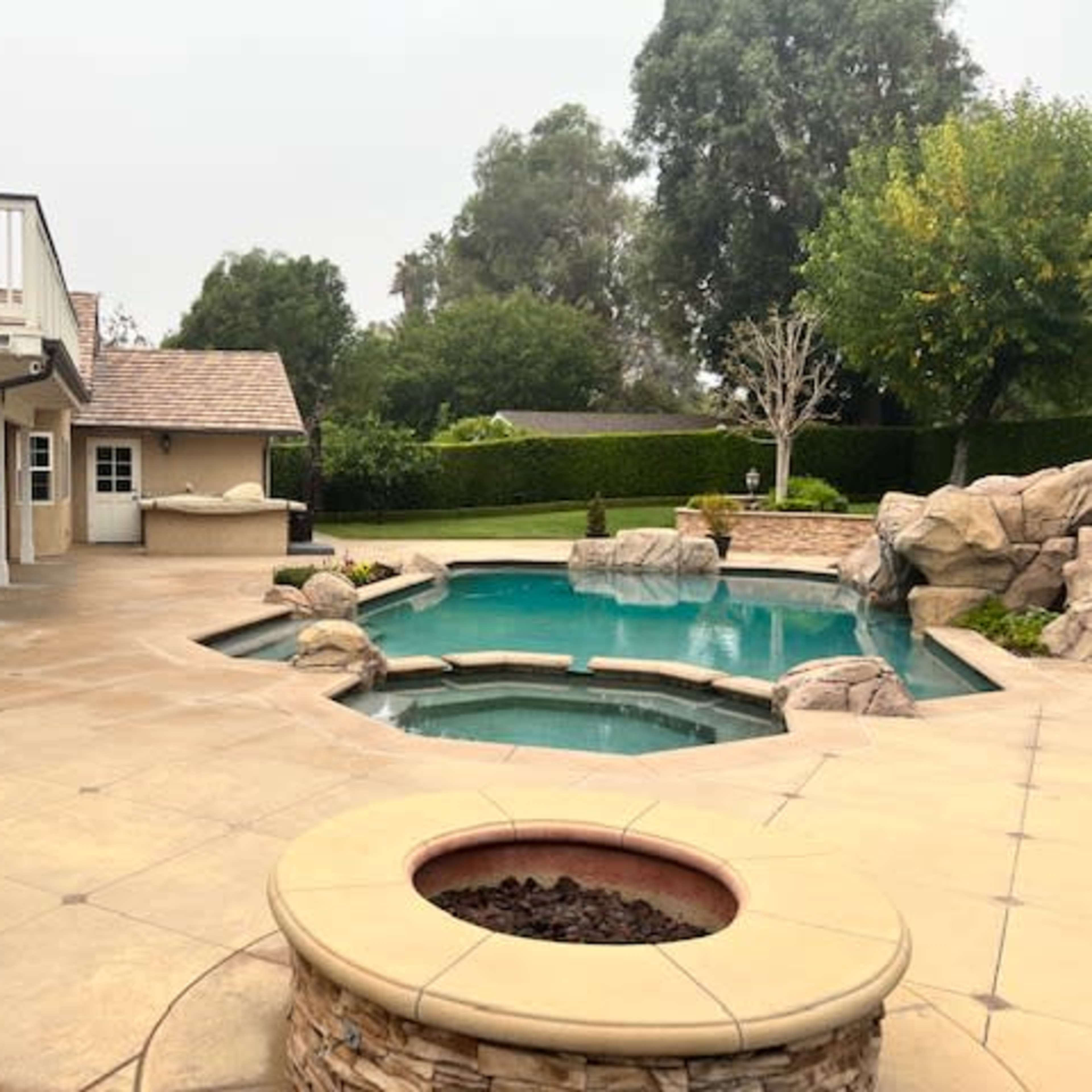 A backyard with a pool, a spa, and a spiral staircase leading to a deck.