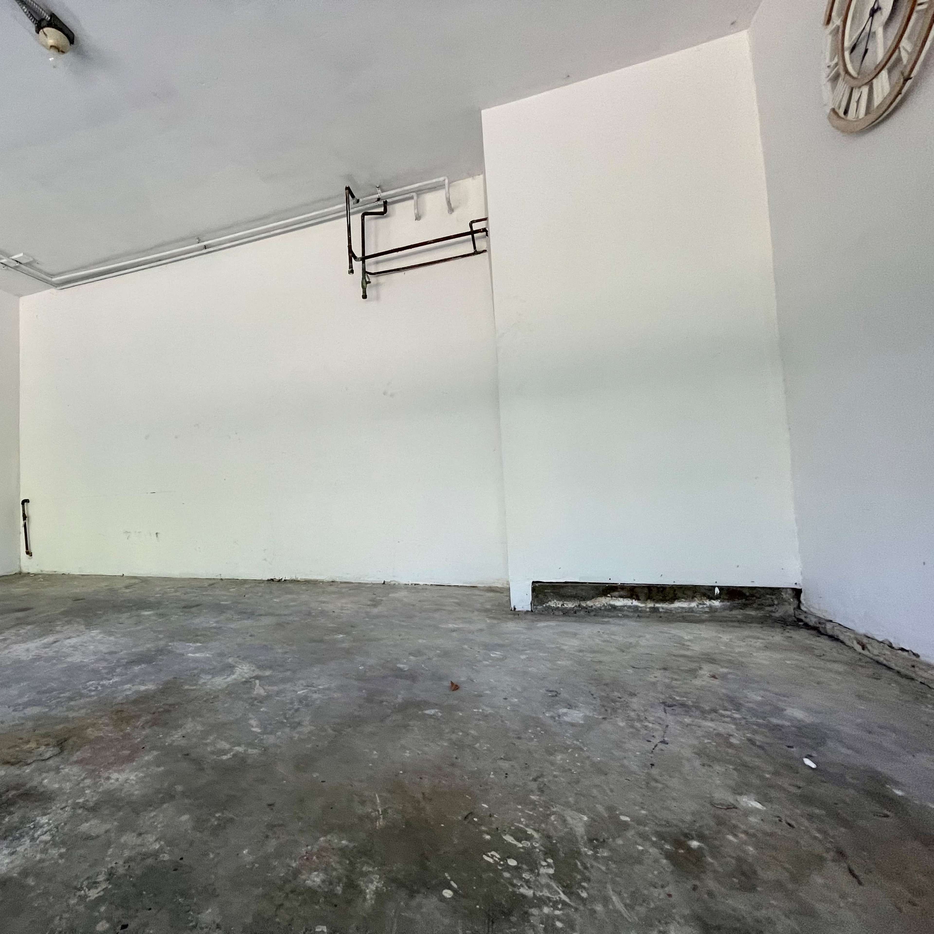 A sparse, unoccupied room with a concrete floor and plain white walls.
