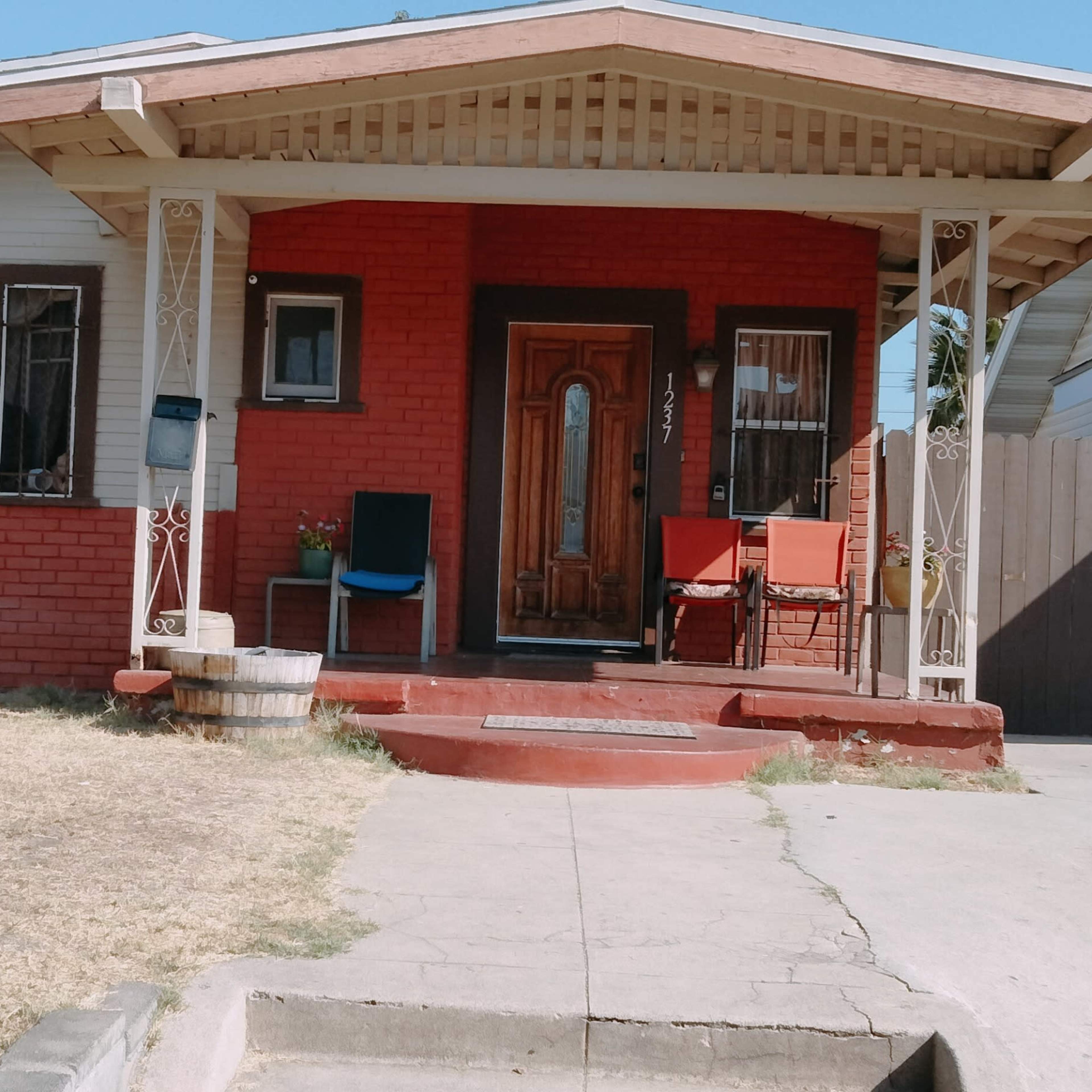 A single-story red brick house with a porch, a small front yard, and a paved walkway leading to the entrance.