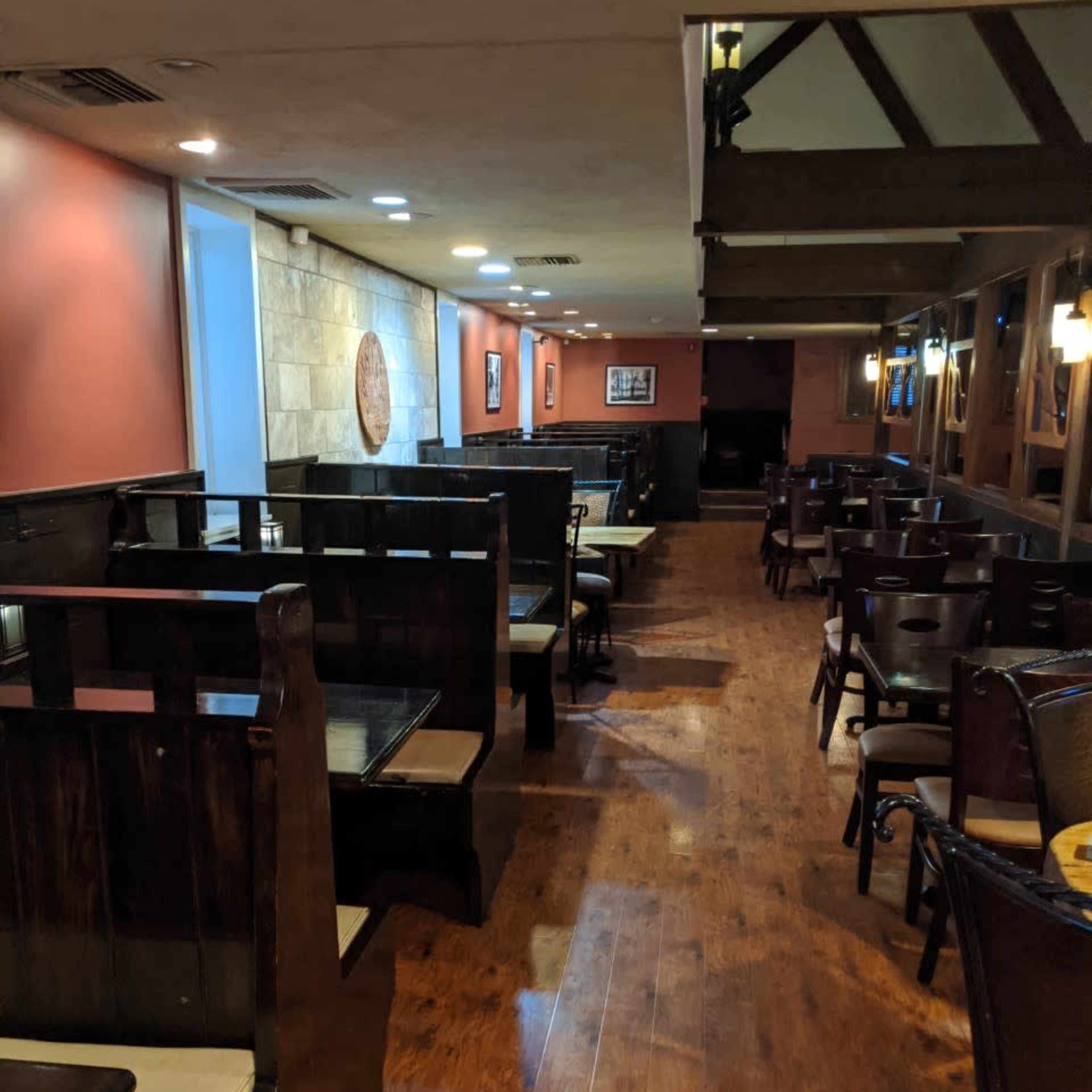 A restaurant interior with wooden booths along the walls and wooden flooring, illuminated by overhead lights.