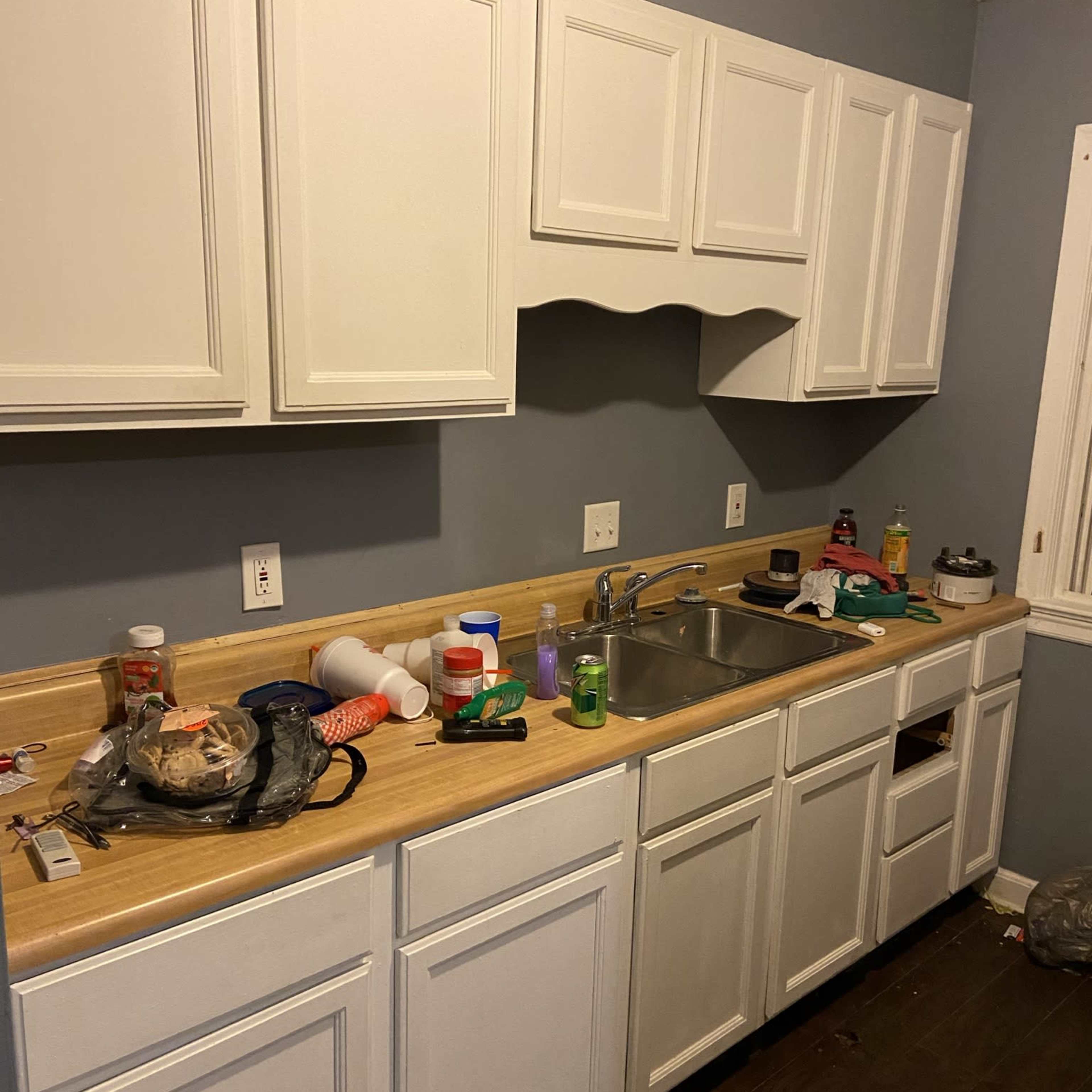 A cluttered kitchen counter with various bottles and containers, beneath white cabinets and a gray wall.