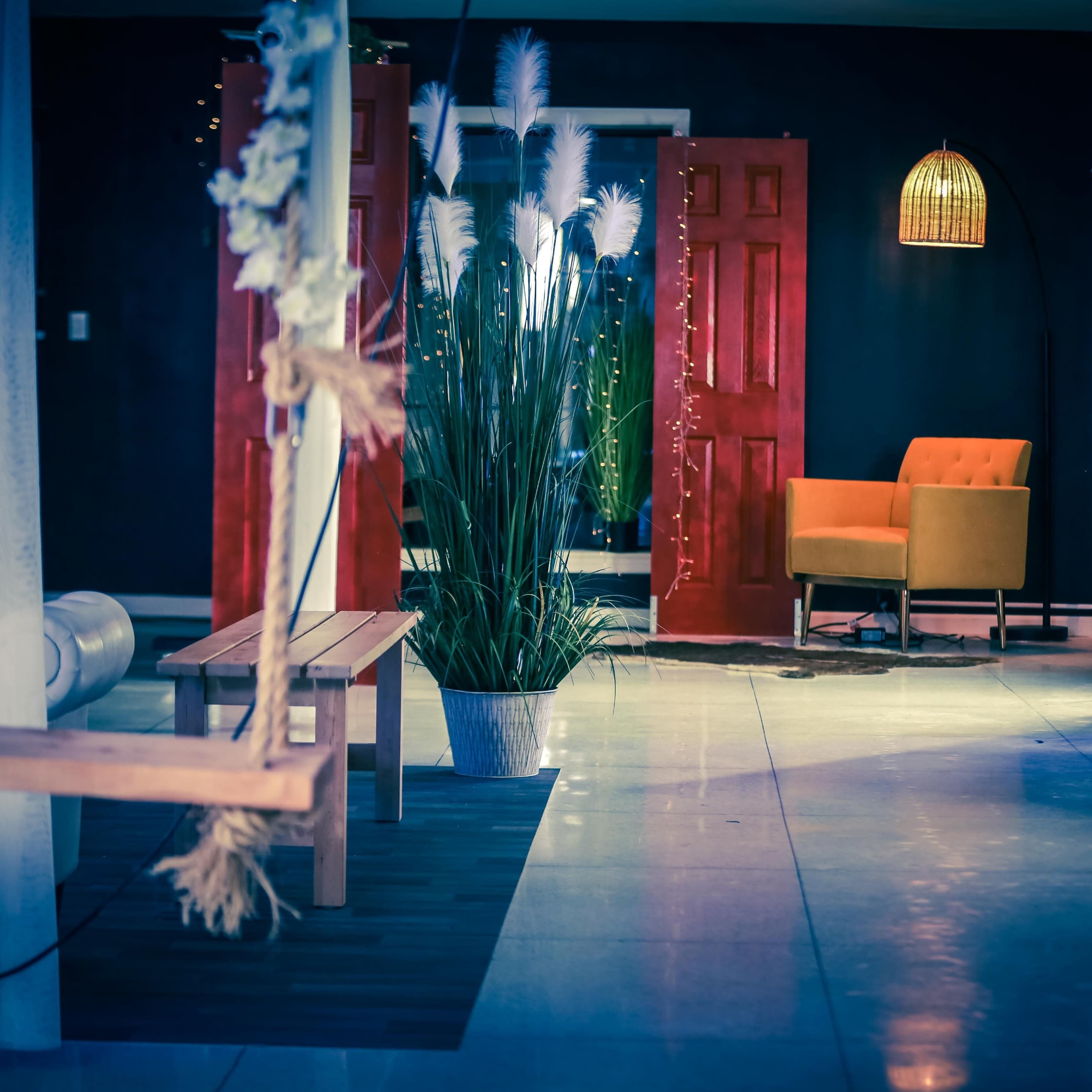 The scene features a modern interior with a vibrant red double door, a cozy orange armchair, and decorative plants, illuminated by soft lighting.