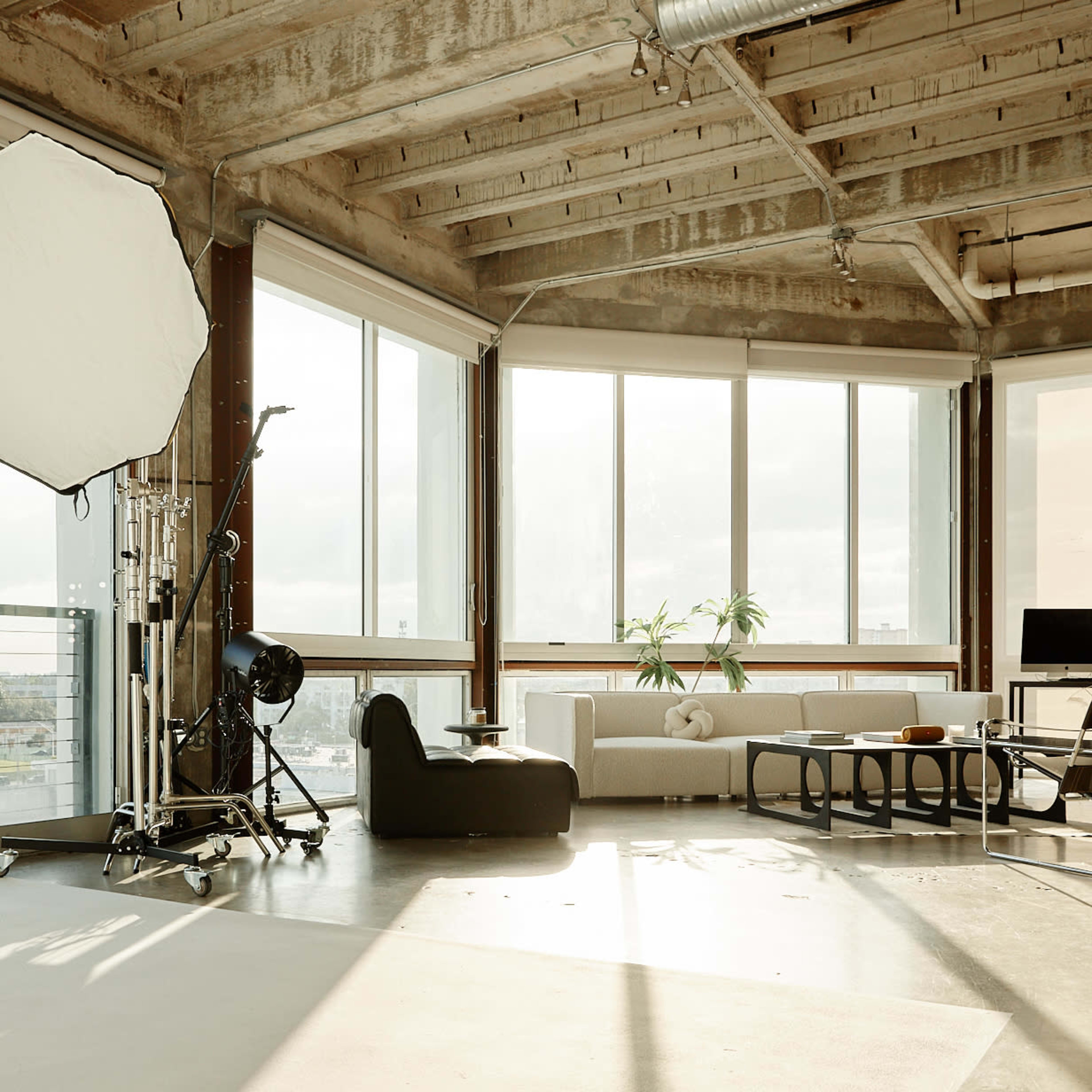 A spacious, industrial-style room features large windows, modern furniture, and equipment for photography.