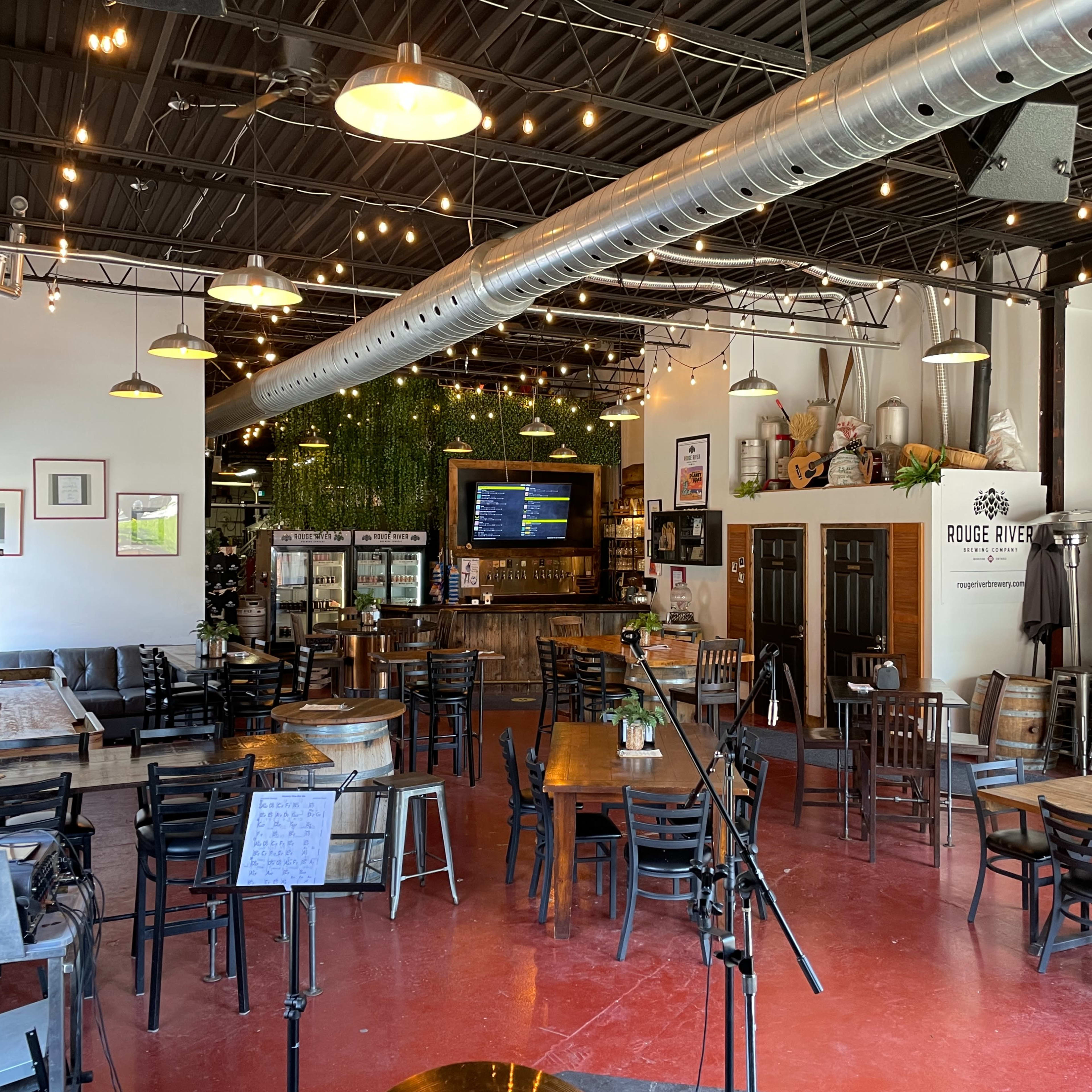 A spacious restaurant interior with wooden tables, chairs, a bar area, and hanging lights.
