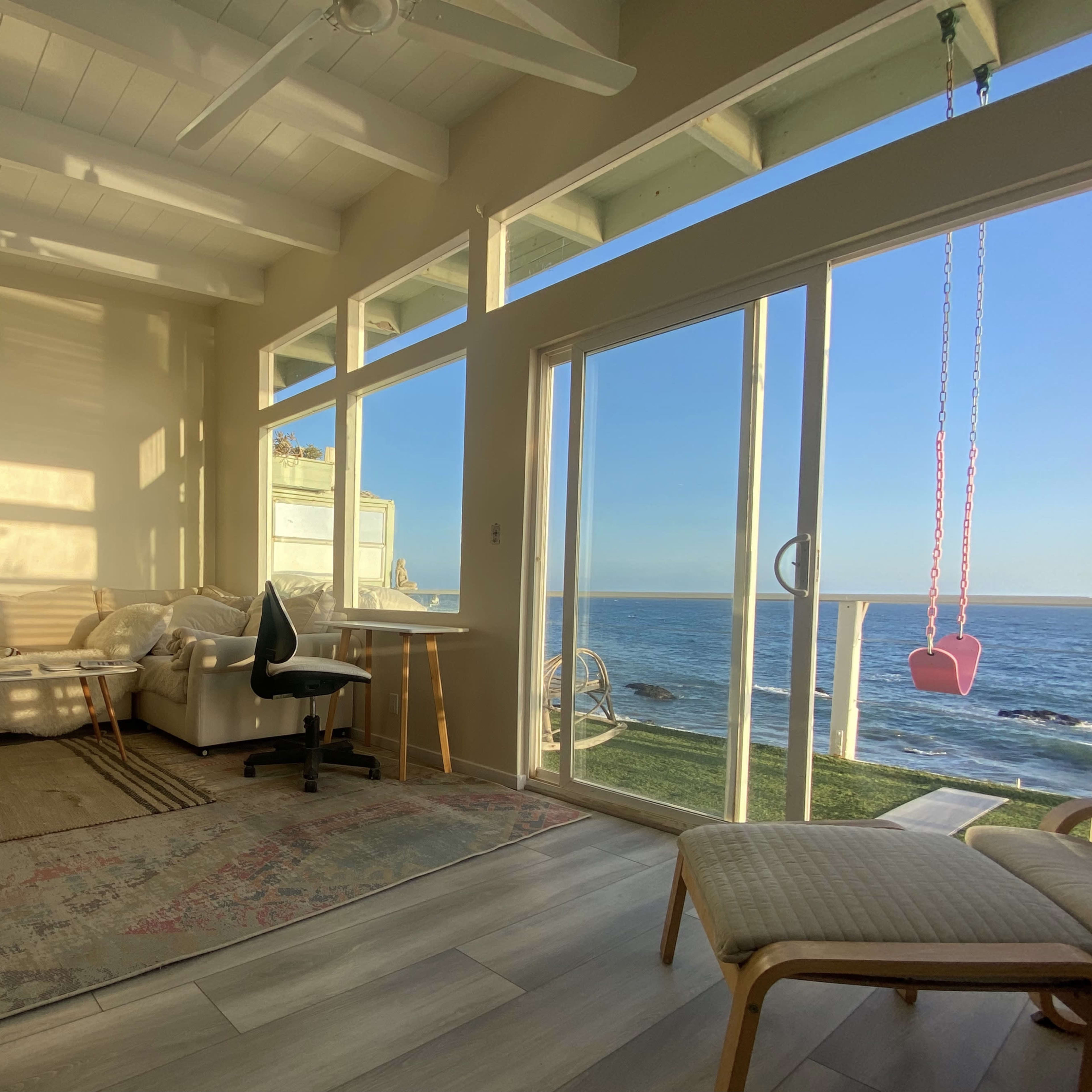 A cozy living space features a bed, a small table with a chair, and large windows overlooking the ocean.