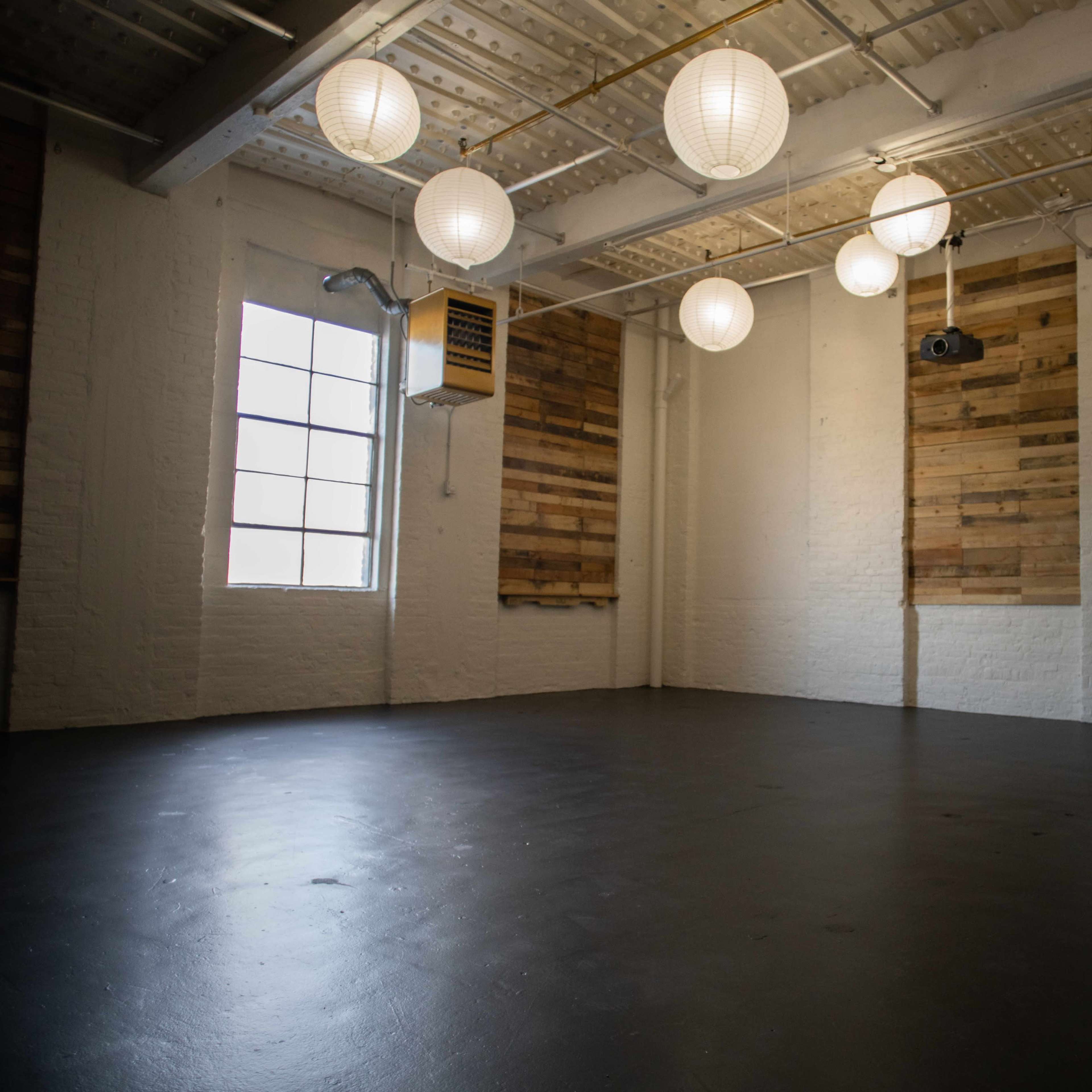 An empty room with wooden wall panels, a large window, and several hanging round lanterns providing illumination.