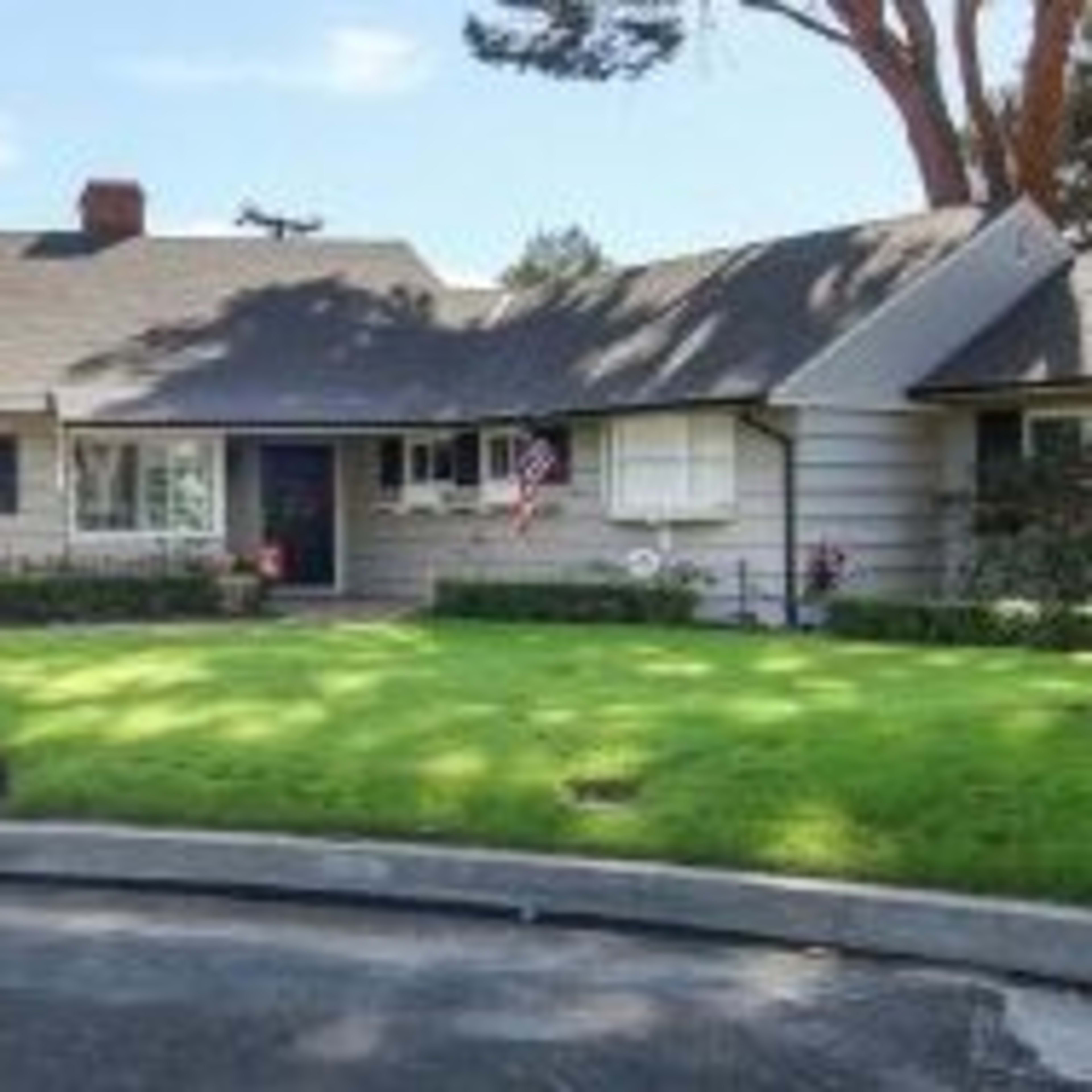 A single-story house with a sloping roof and a front yard, featuring a mailbox and a curved driveway.