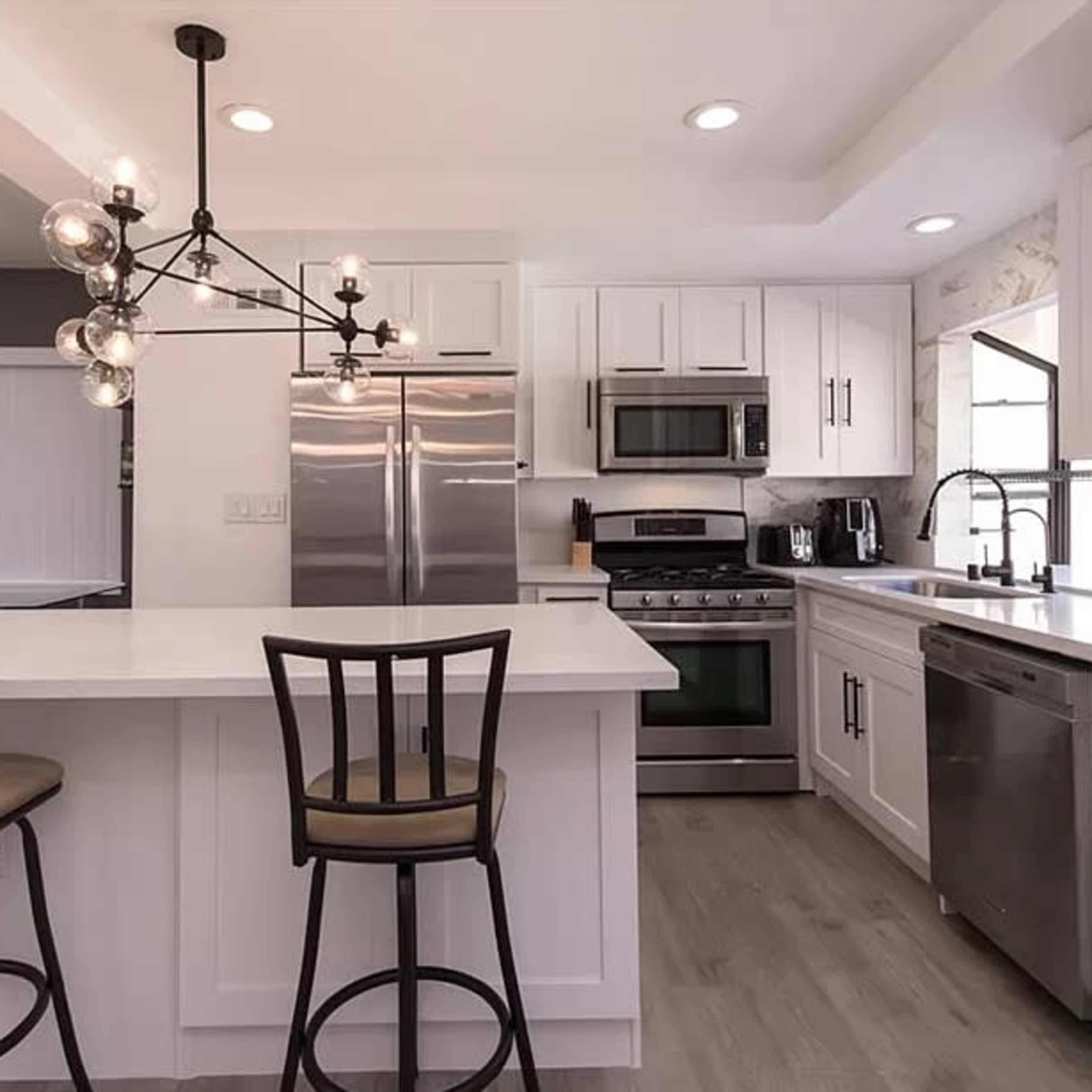 A modern kitchen features white cabinetry, stainless steel appliances, and a center island with two bar stools.