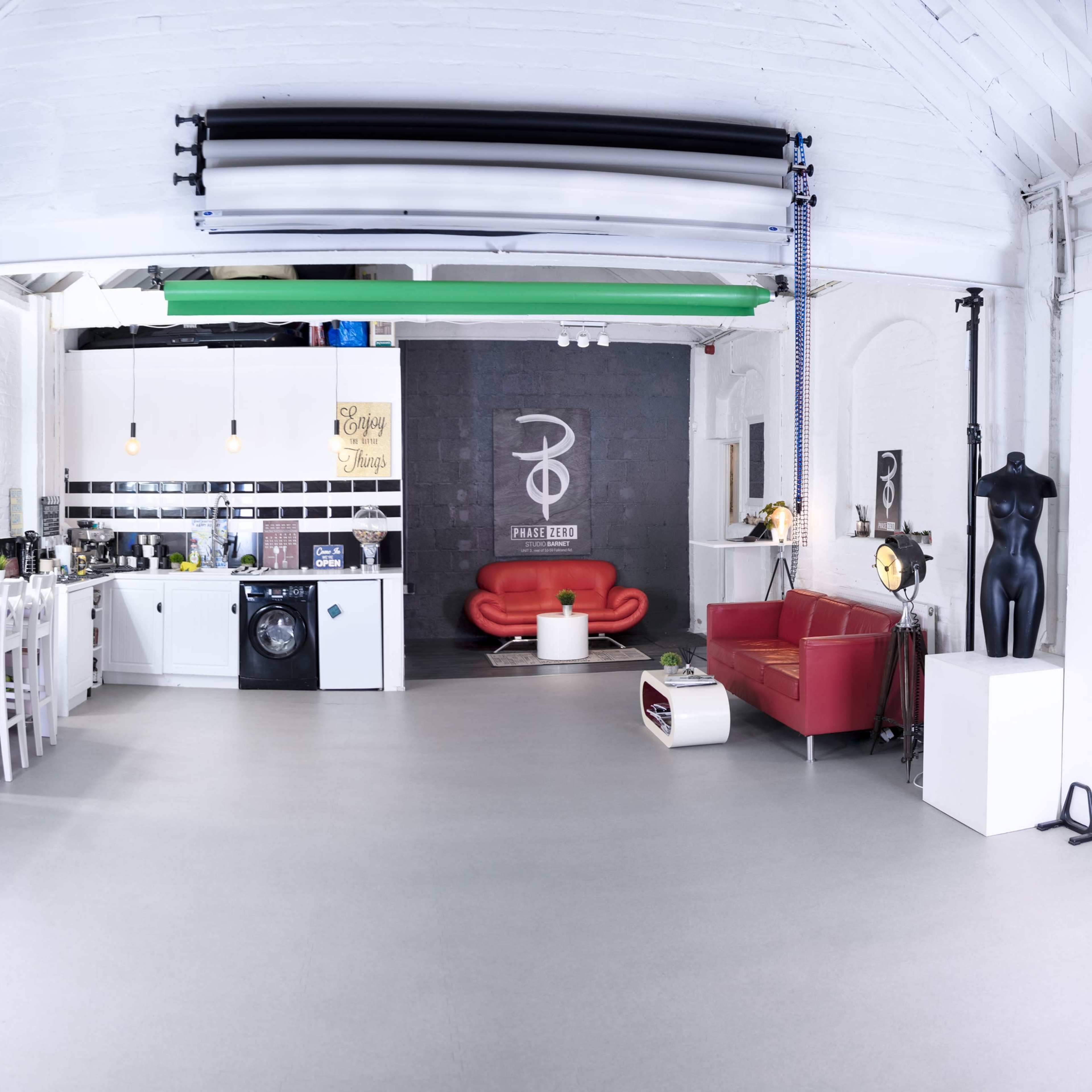 A spacious, white-walled studio featuring a kitchen area, a red sofa, a black mannequin, and various colorful backdrops along one wall.