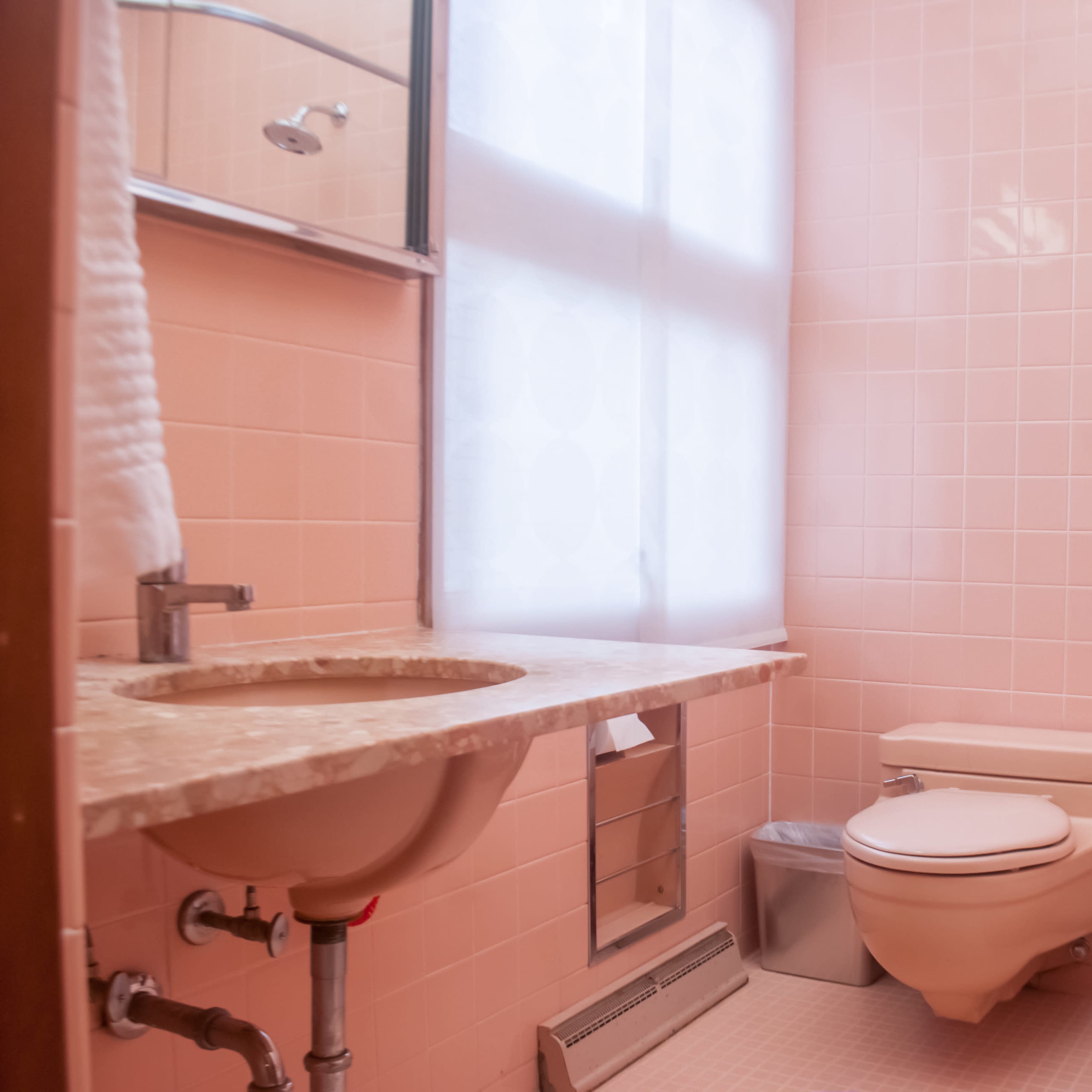 A bathroom features pink tiled walls, a marble countertop sink, a toilet, and a tub with a showerhead.