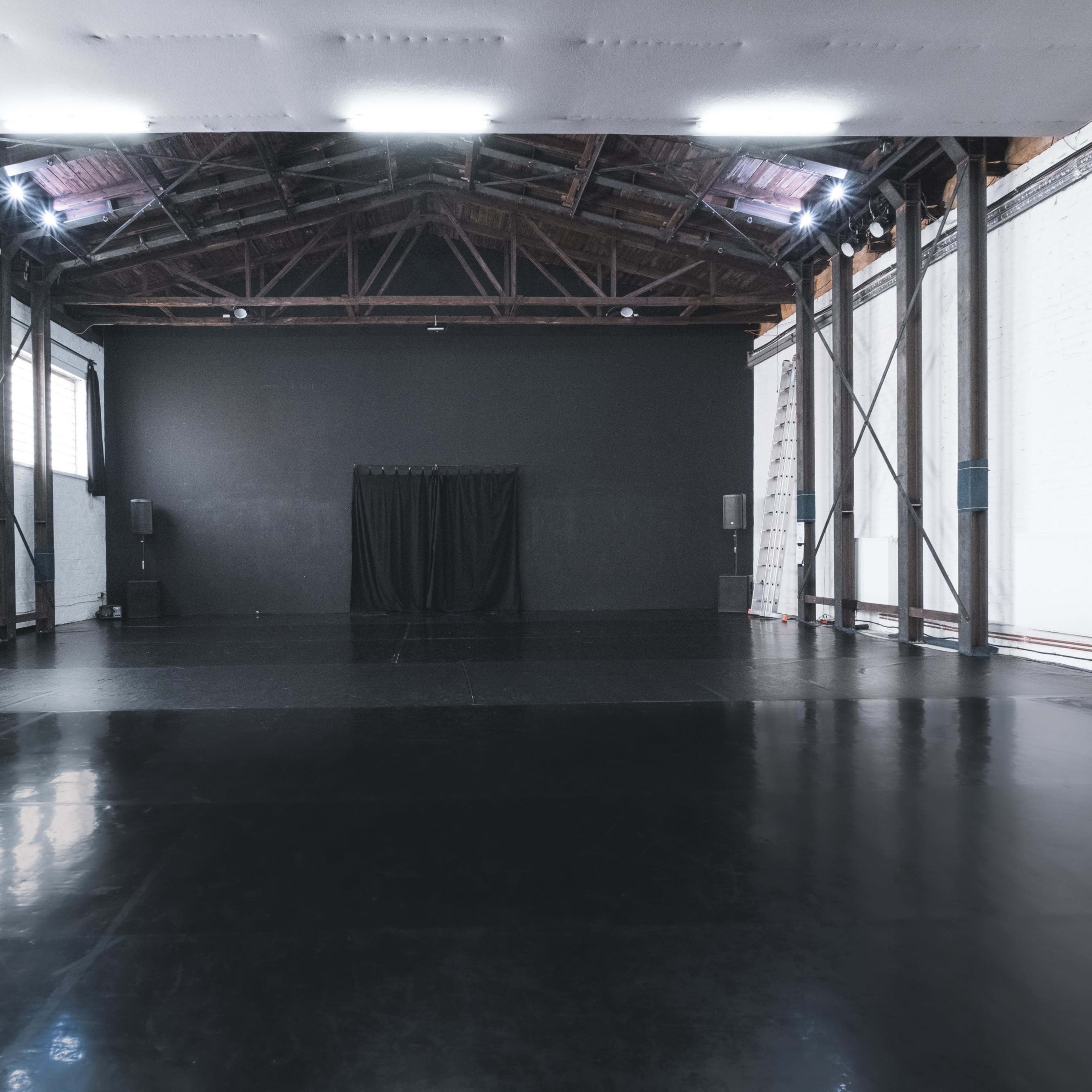 A large, empty studio space with polished black flooring and high wooden beams.
