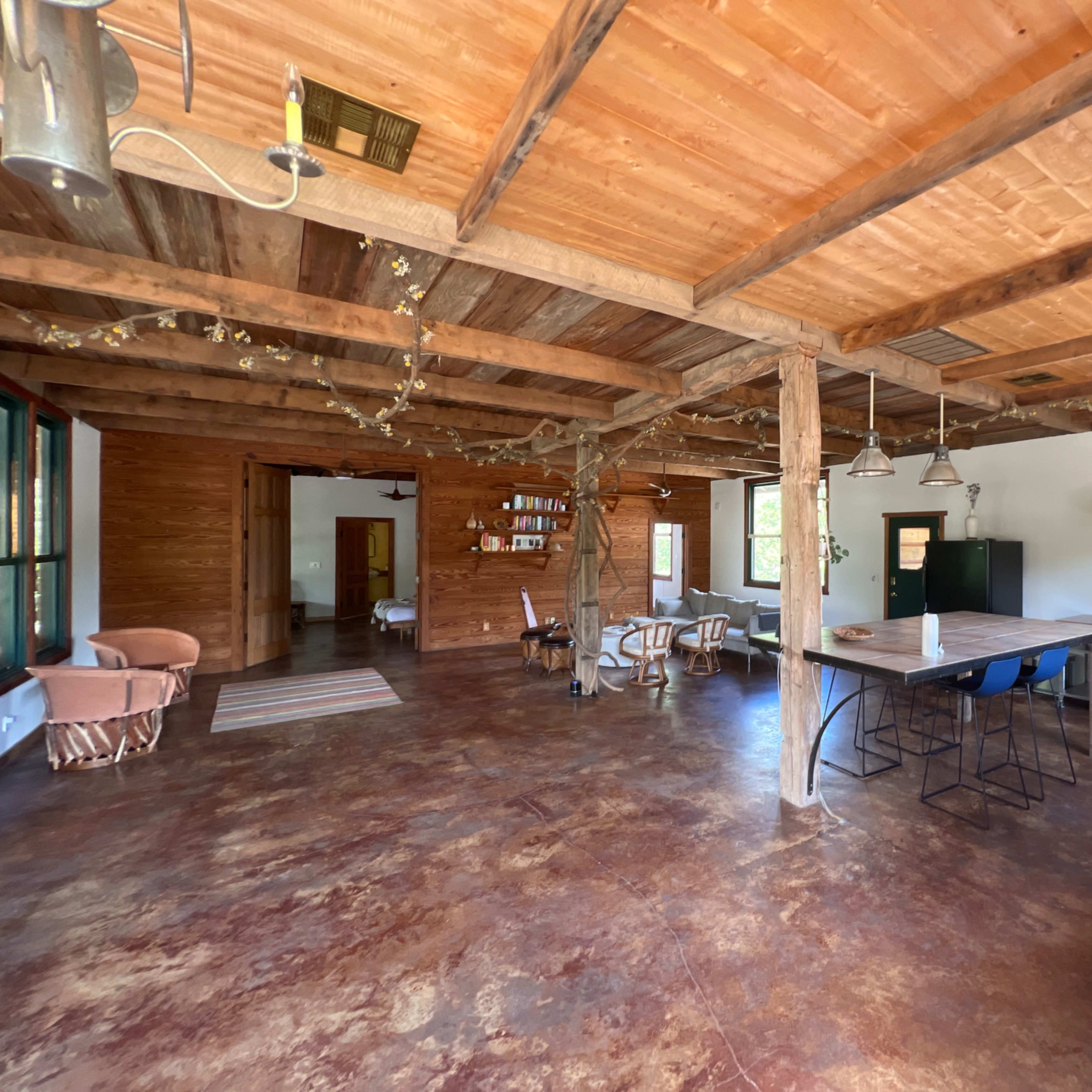 An open-concept interior of a rustic living space featuring wooden ceilings, a kitchen area with modern appliances, and seating arrangements.