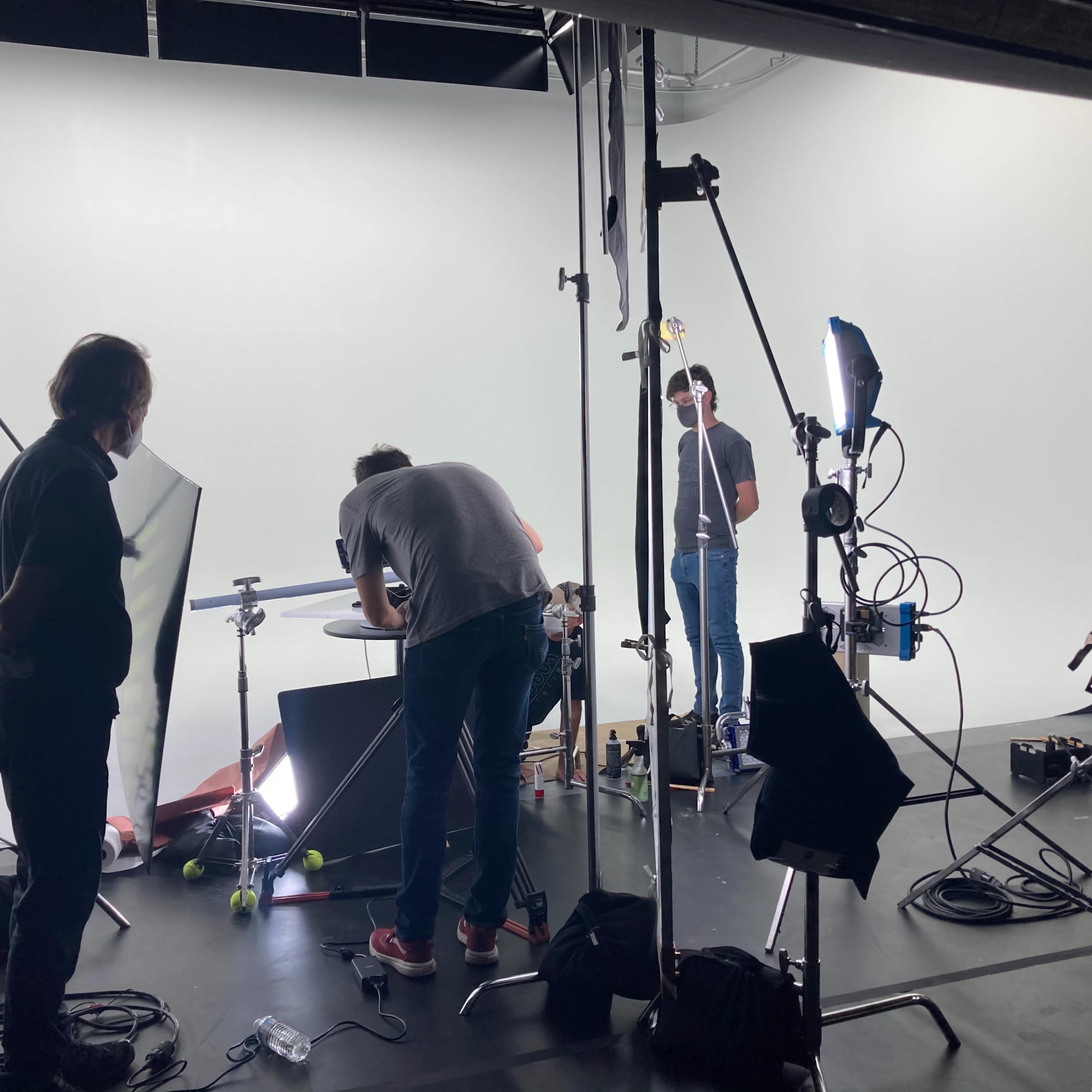 A group of people is setting up equipment in a studio with a white backdrop.
