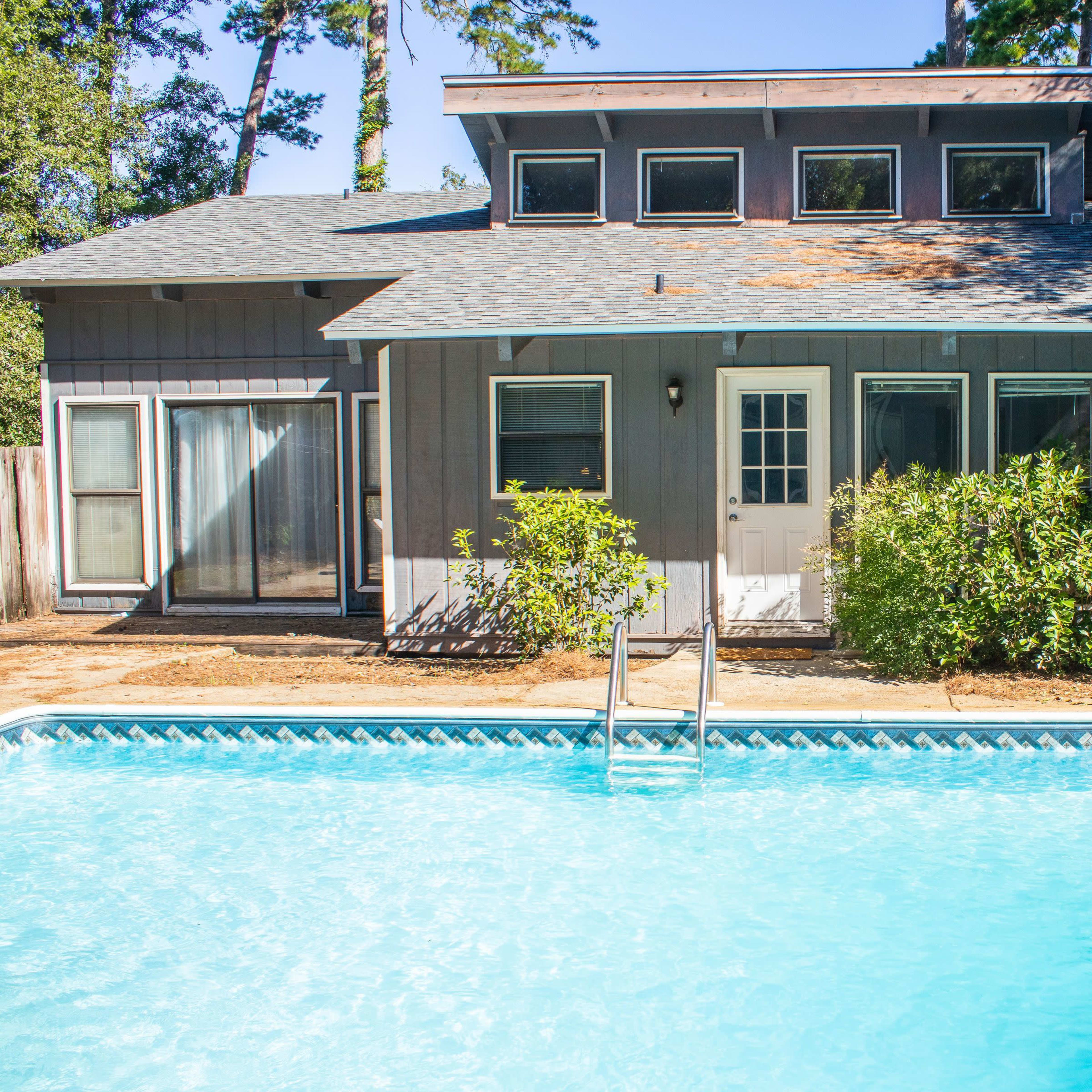 A two-story house with large windows and a swimming pool in the front yard.