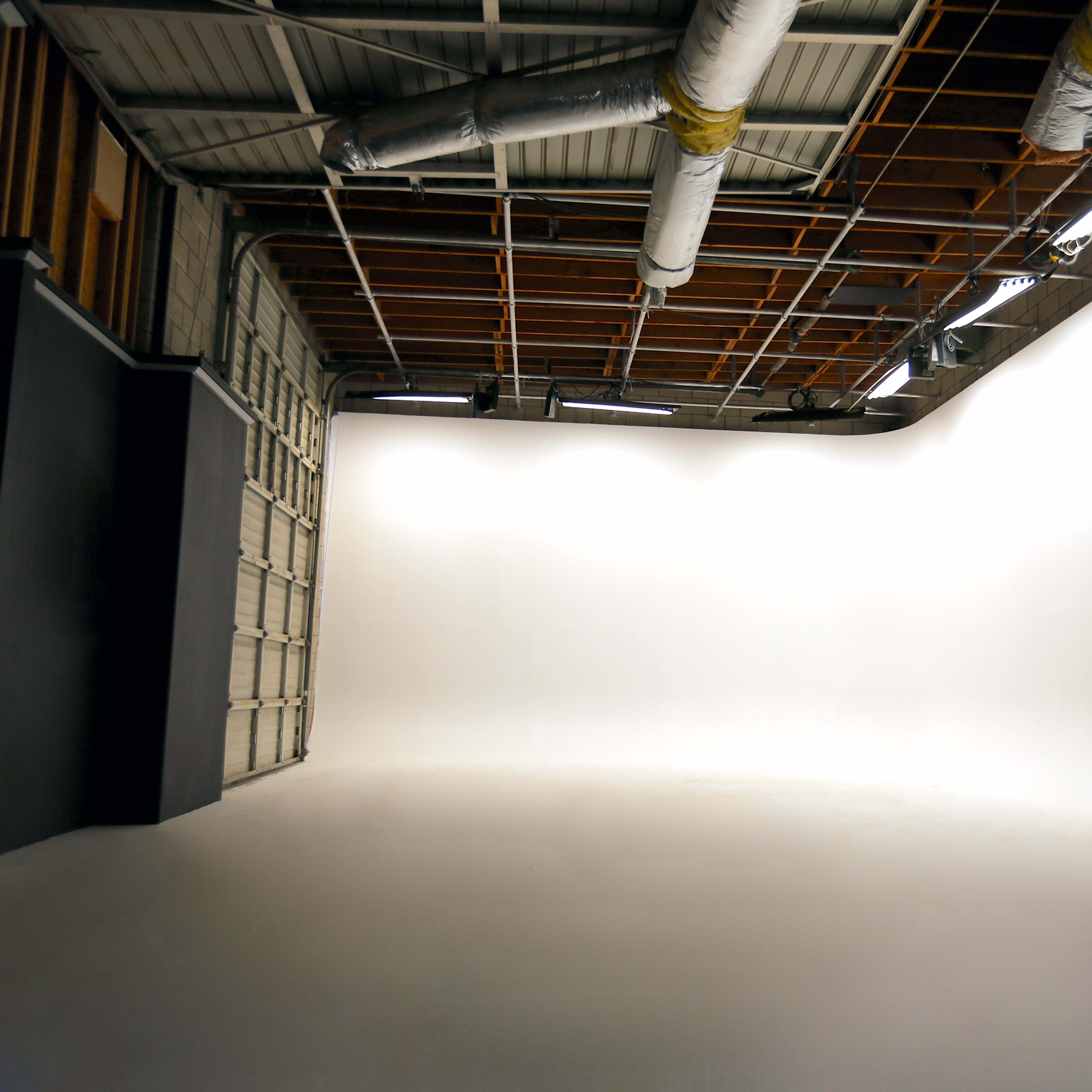 A spacious, empty photography studio with a large seamless white backdrop and exposed ceiling features.