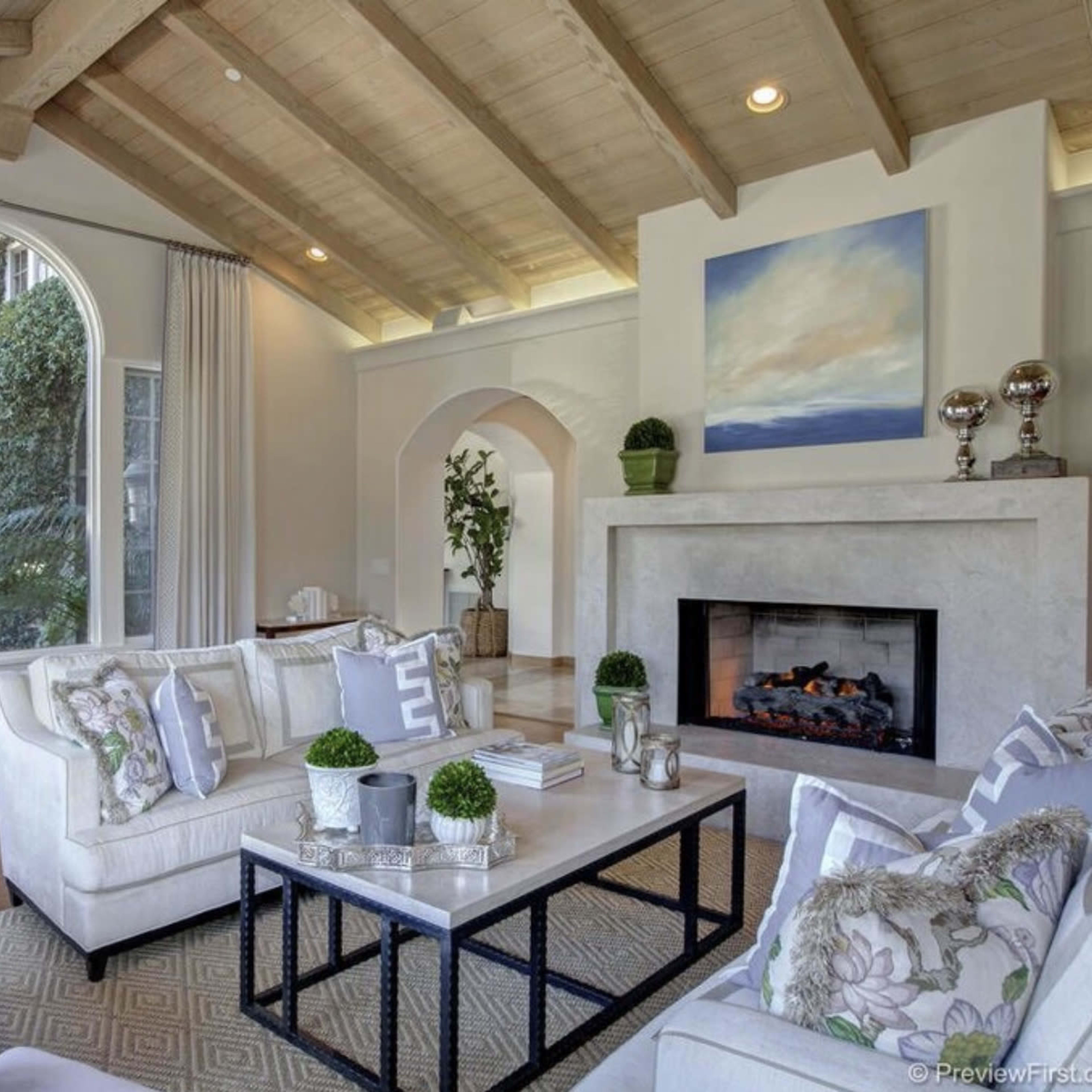 The living room features a vaulted ceiling, large windows, a fireplace, and a mix of comfortable seating arrangements.
