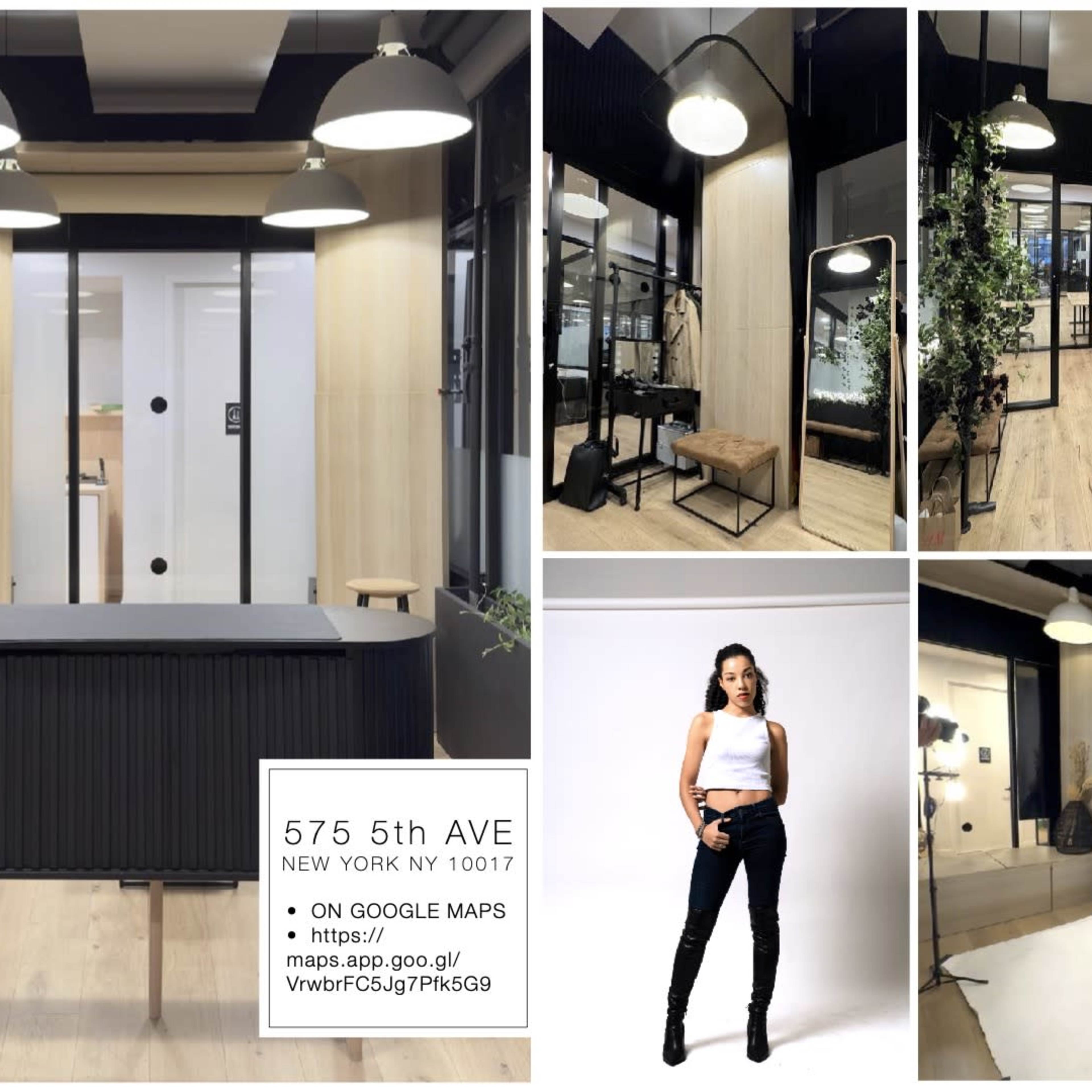 A modern workspace with an open layout, featuring a reception area, private meeting rooms, and stylish decor, along with a display of clothing and photography equipment.