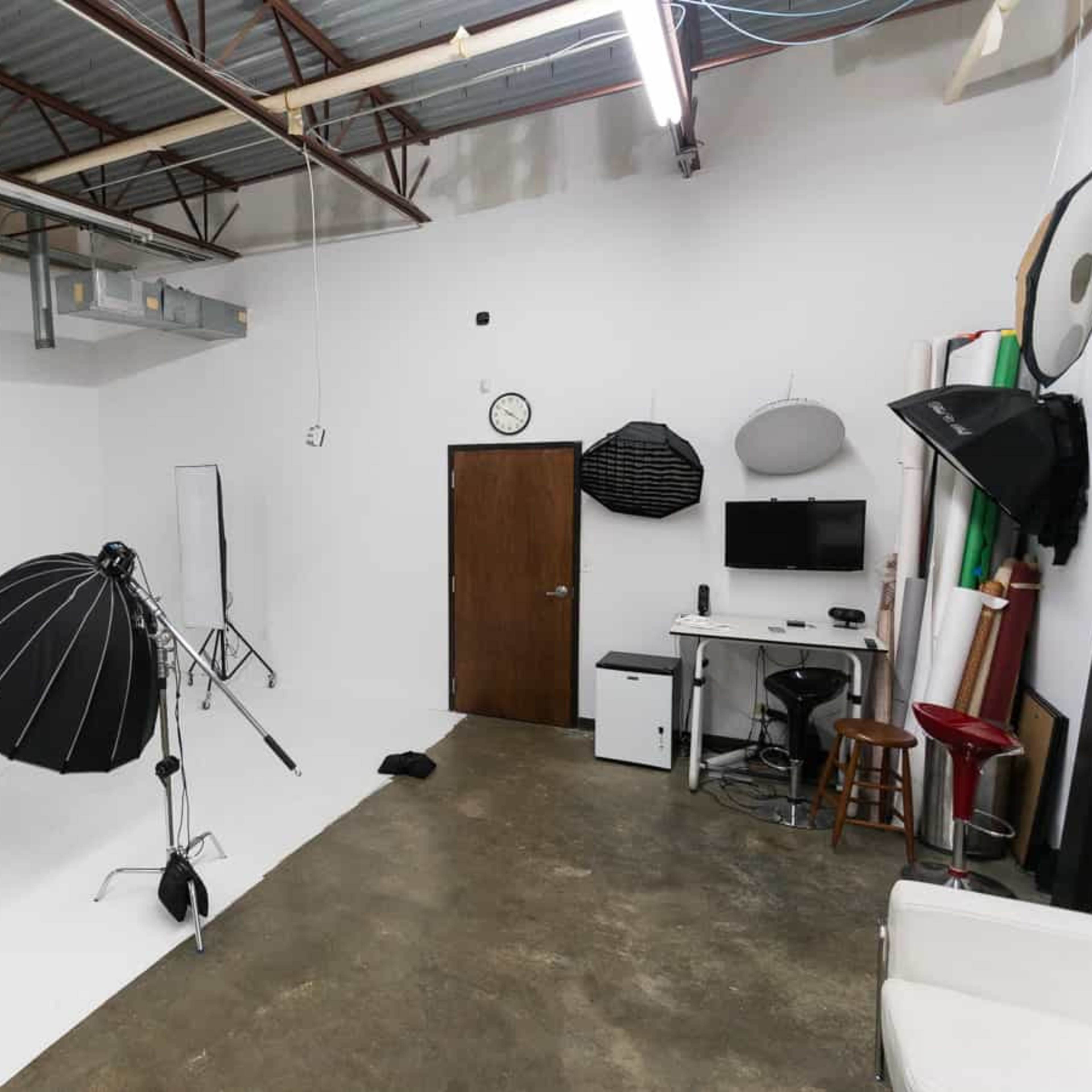 A photography studio with equipment such as softboxes, a backdrop, and a desk with a monitor.