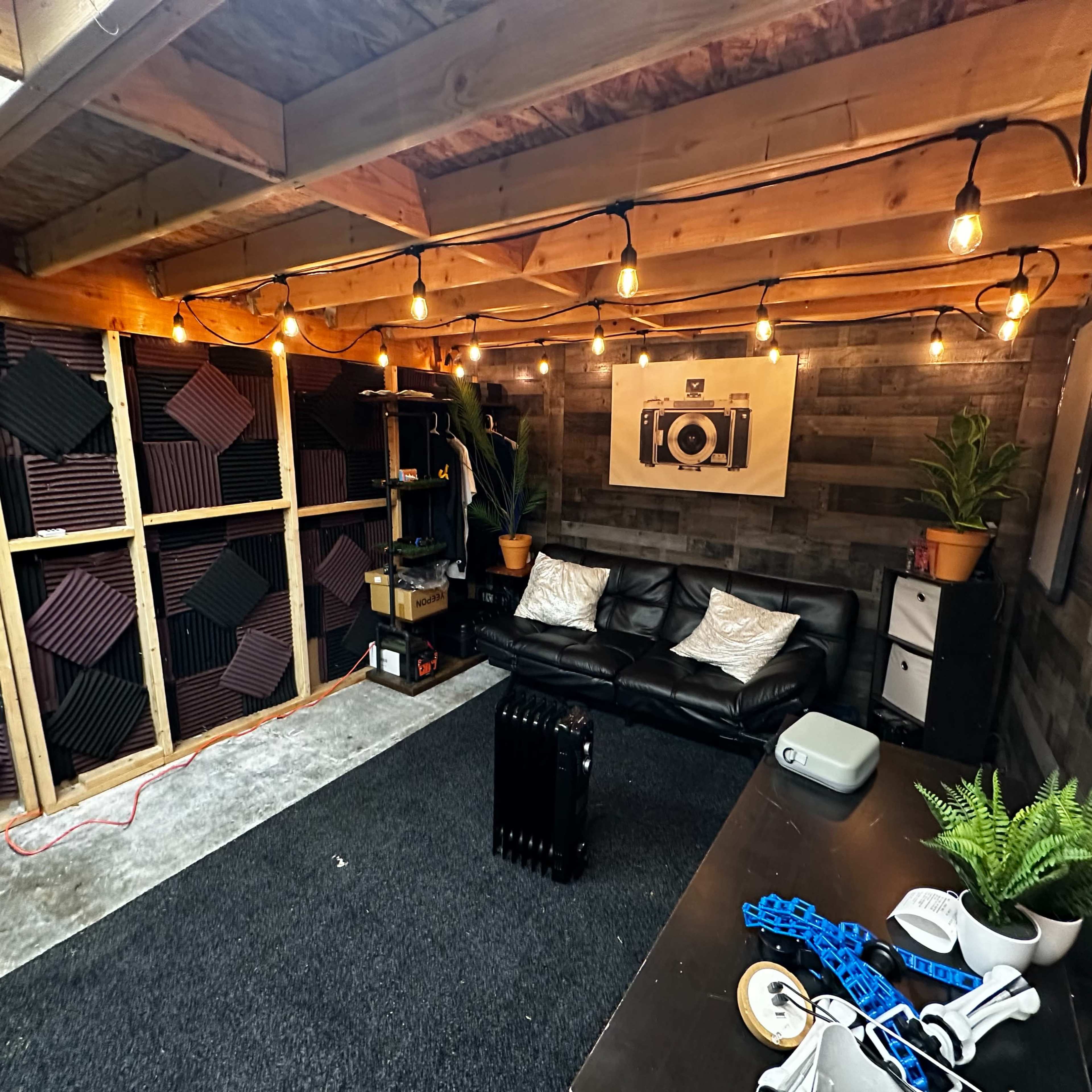 A soundproof room featuring dark walls, a couch, acoustic panels on the left, and a projector on a table.