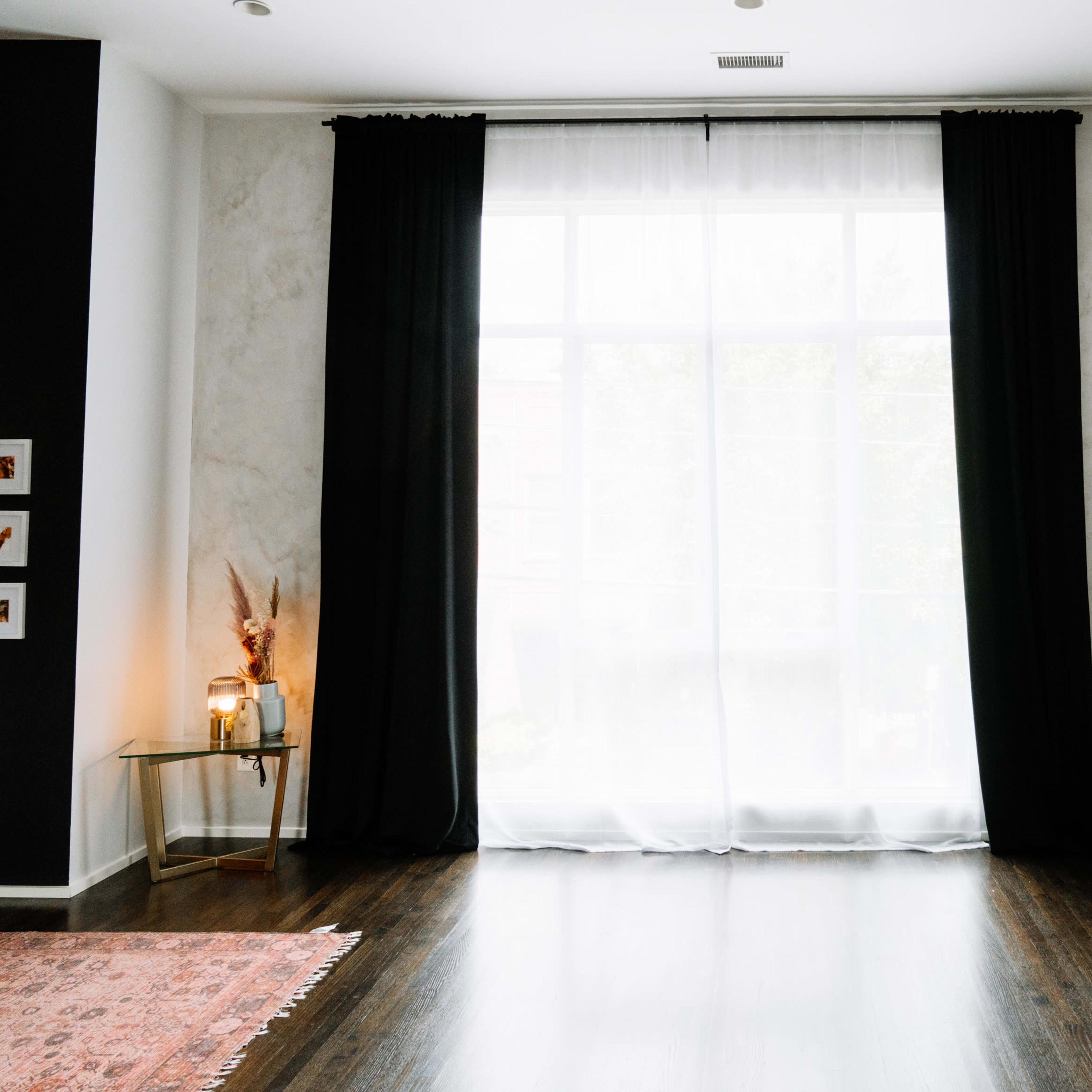 A minimalist interior features a curved bench, a round mirror, and a large window partially covered by black curtains.