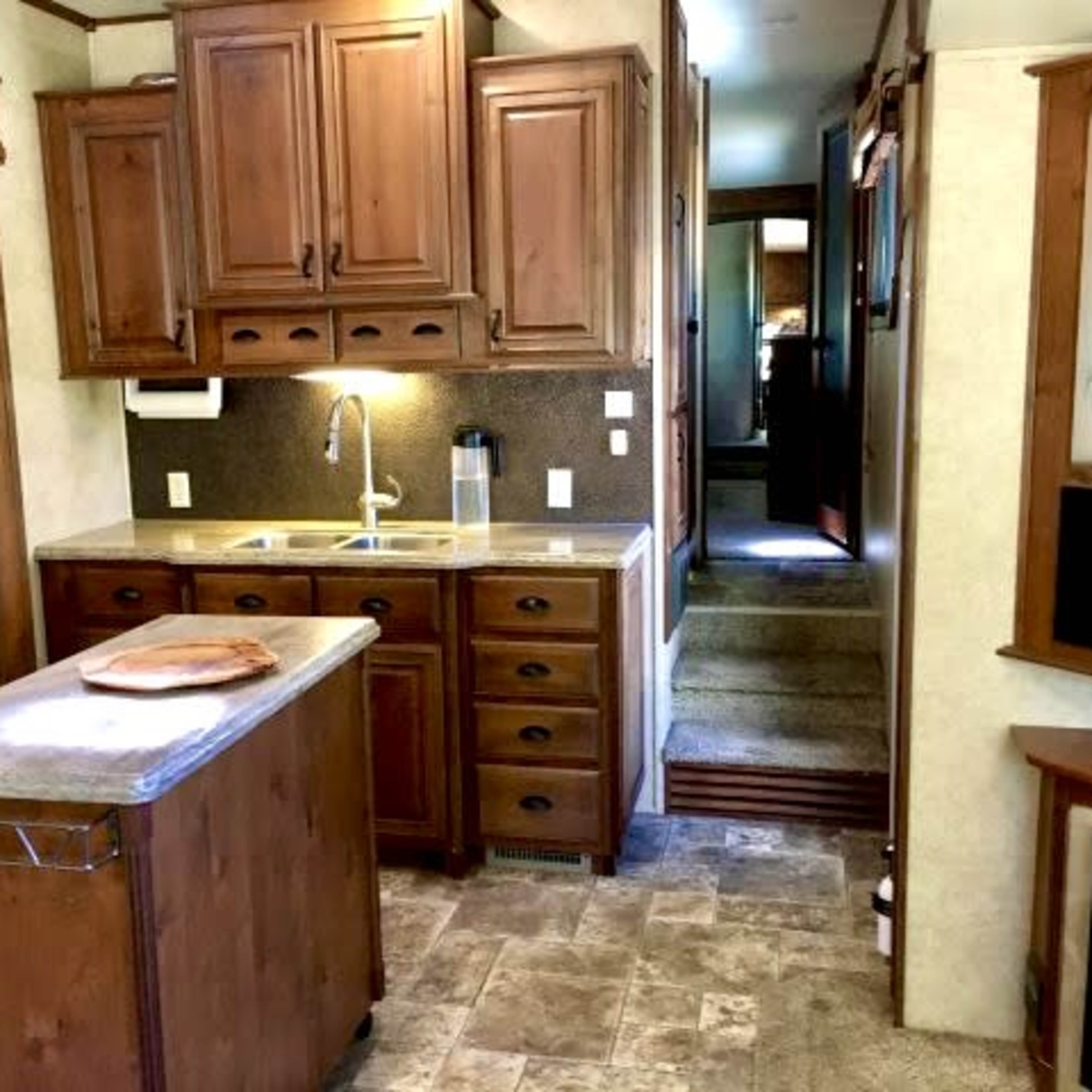 A kitchen with wooden cabinets, a countertop island, and appliances, set within a travel trailer.
