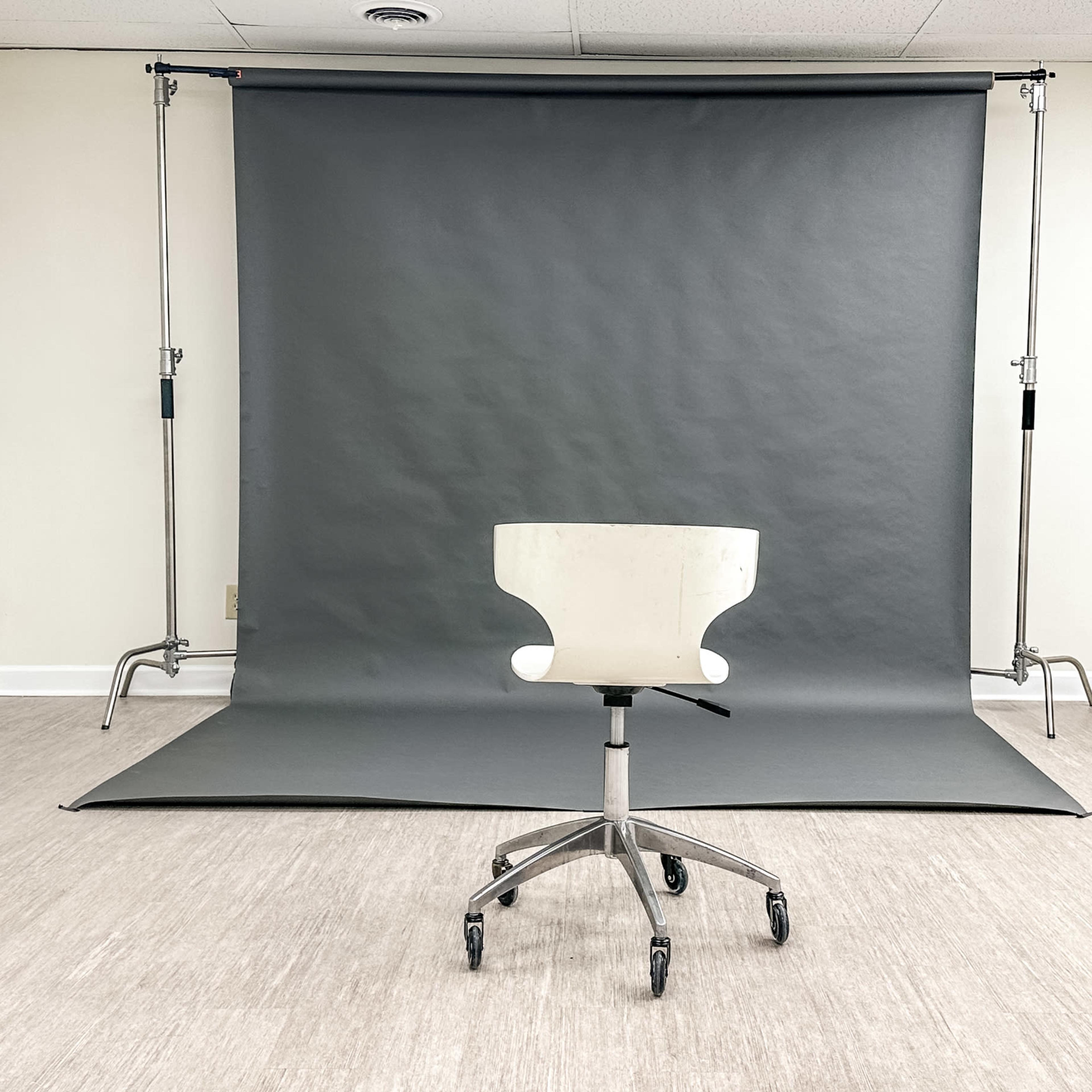 A white office chair on wheels sits in front of a gray backdrop set up on a clean, light-colored floor.