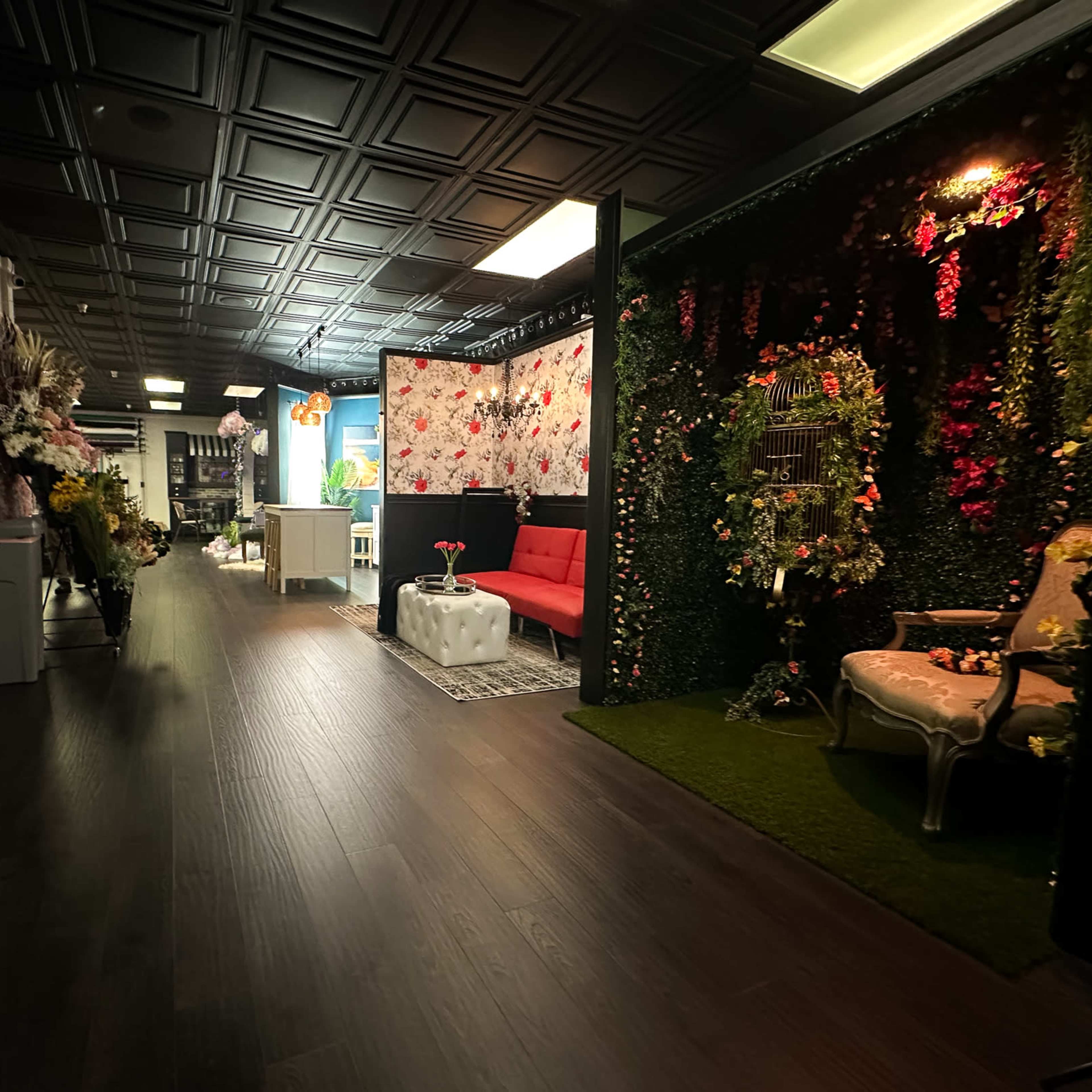 A hallway with lockers on one side, leading to a decorated space featuring a red couch, floral wallpaper, and greenery.