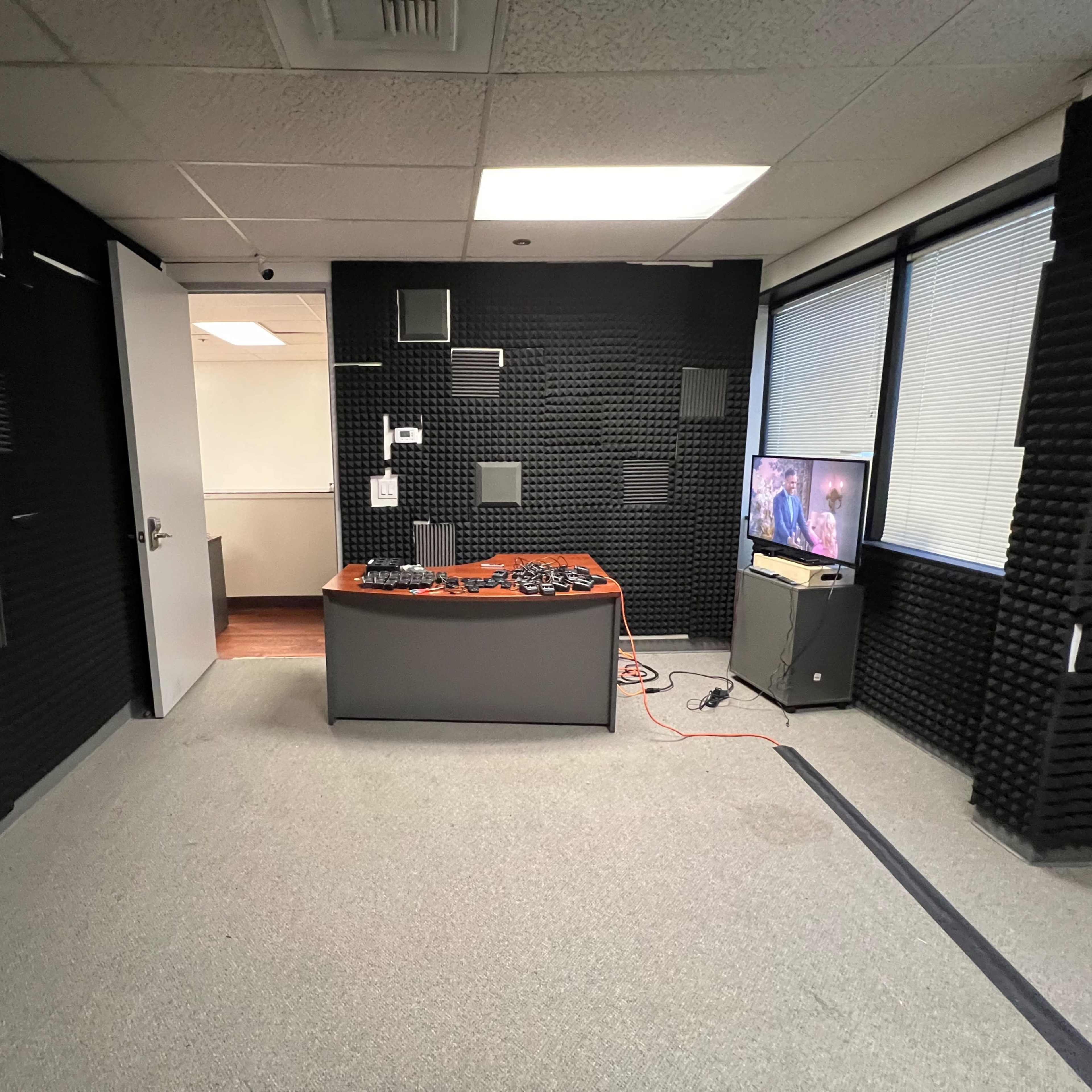 A soundproof room with black acoustic foam panels on the walls, a gray carpet, and a table displaying various tools or equipment.