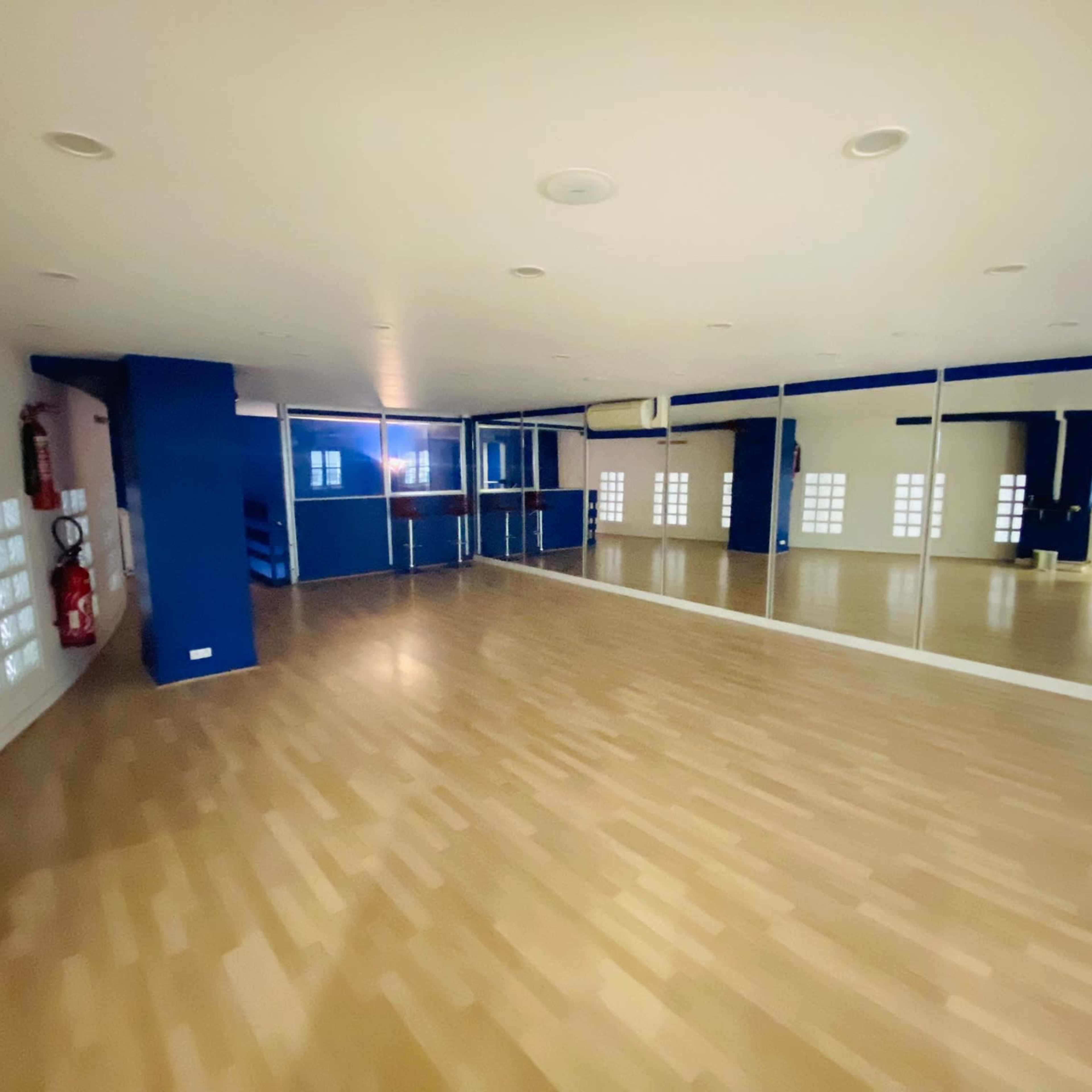 A spacious, empty room with wooden flooring and large mirrors along one wall, featuring blue accents and glass block windows.