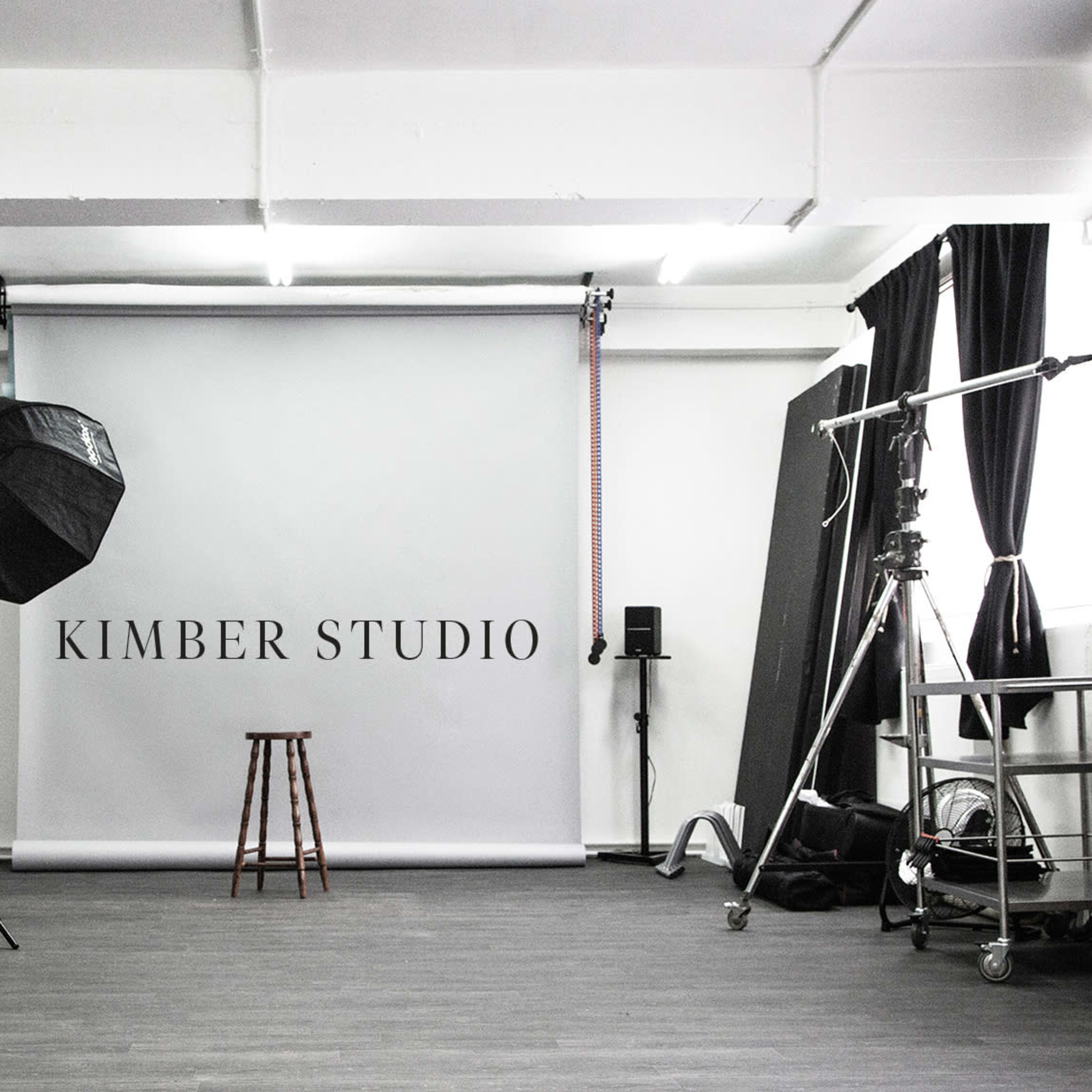 A photography studio with a plain backdrop, a stool, lighting equipment, and various studio furniture arranged neatly.