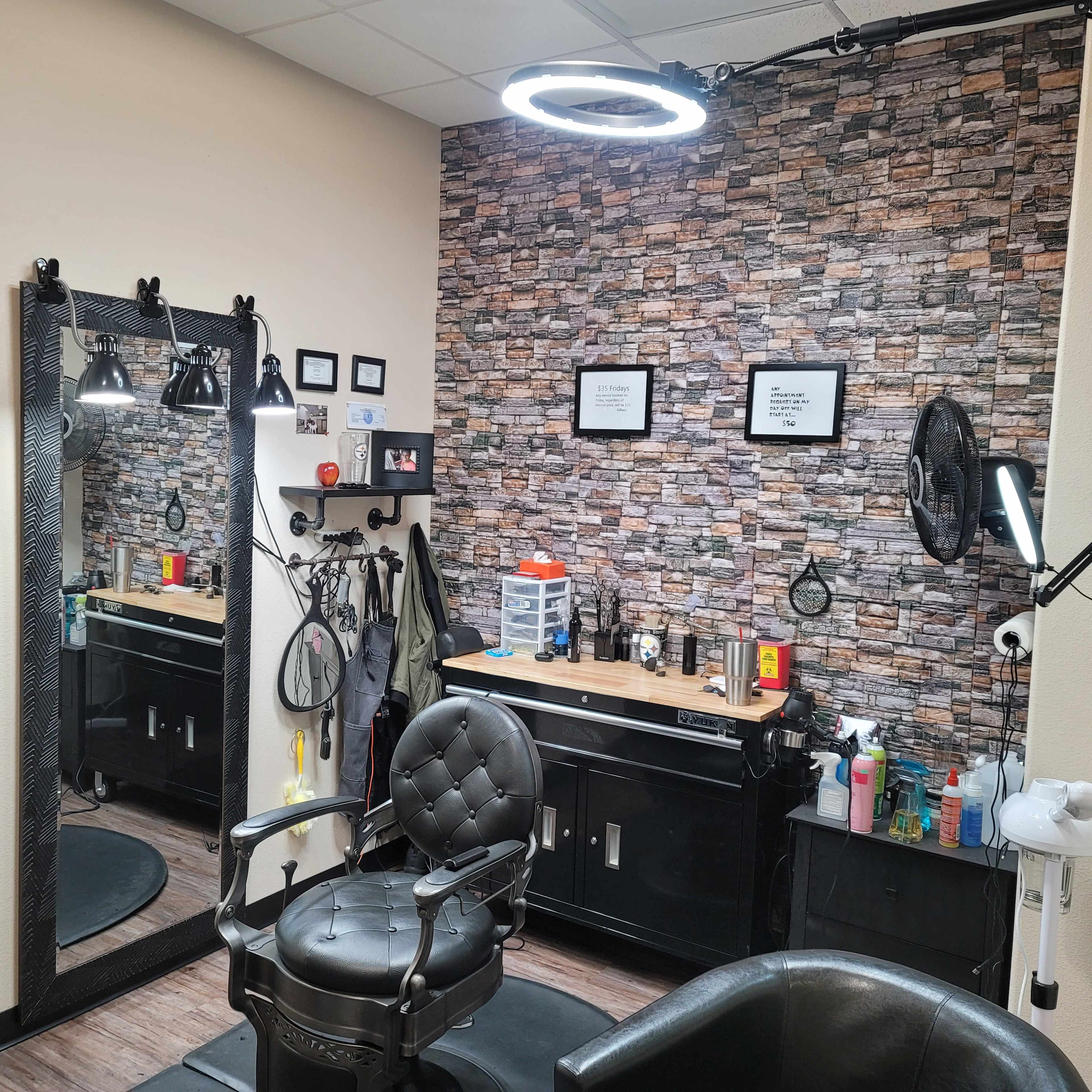 A small hair salon with a black barber chair, a large mirror, and a stone-patterned accent wall, equipped with various salon products and tools.