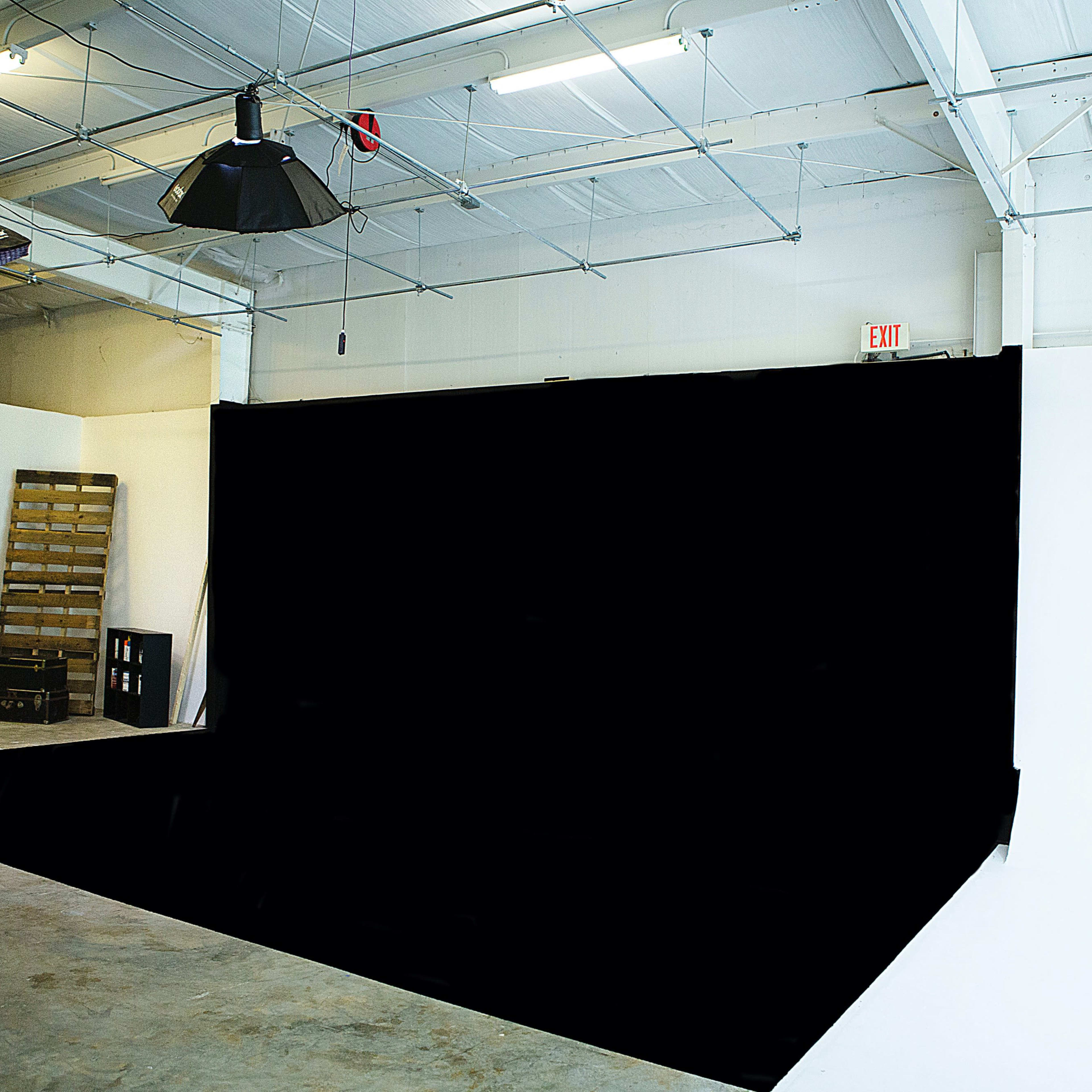 A spacious studio with a black backdrop, concrete flooring, and various lighting fixtures hanging from the ceiling.