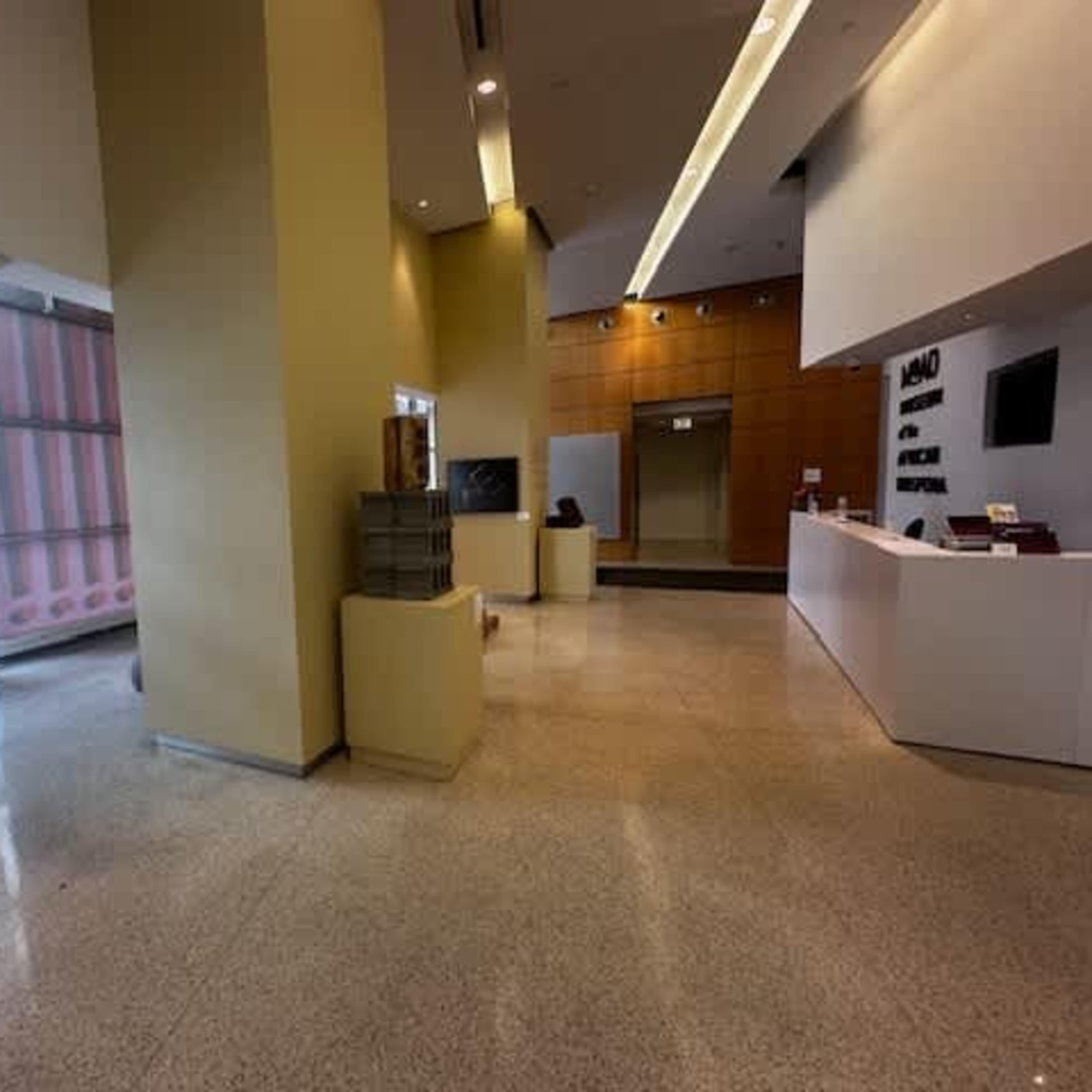 A spacious, modern lobby area with a reception desk, a staircase, and large windows allowing natural light to enter.