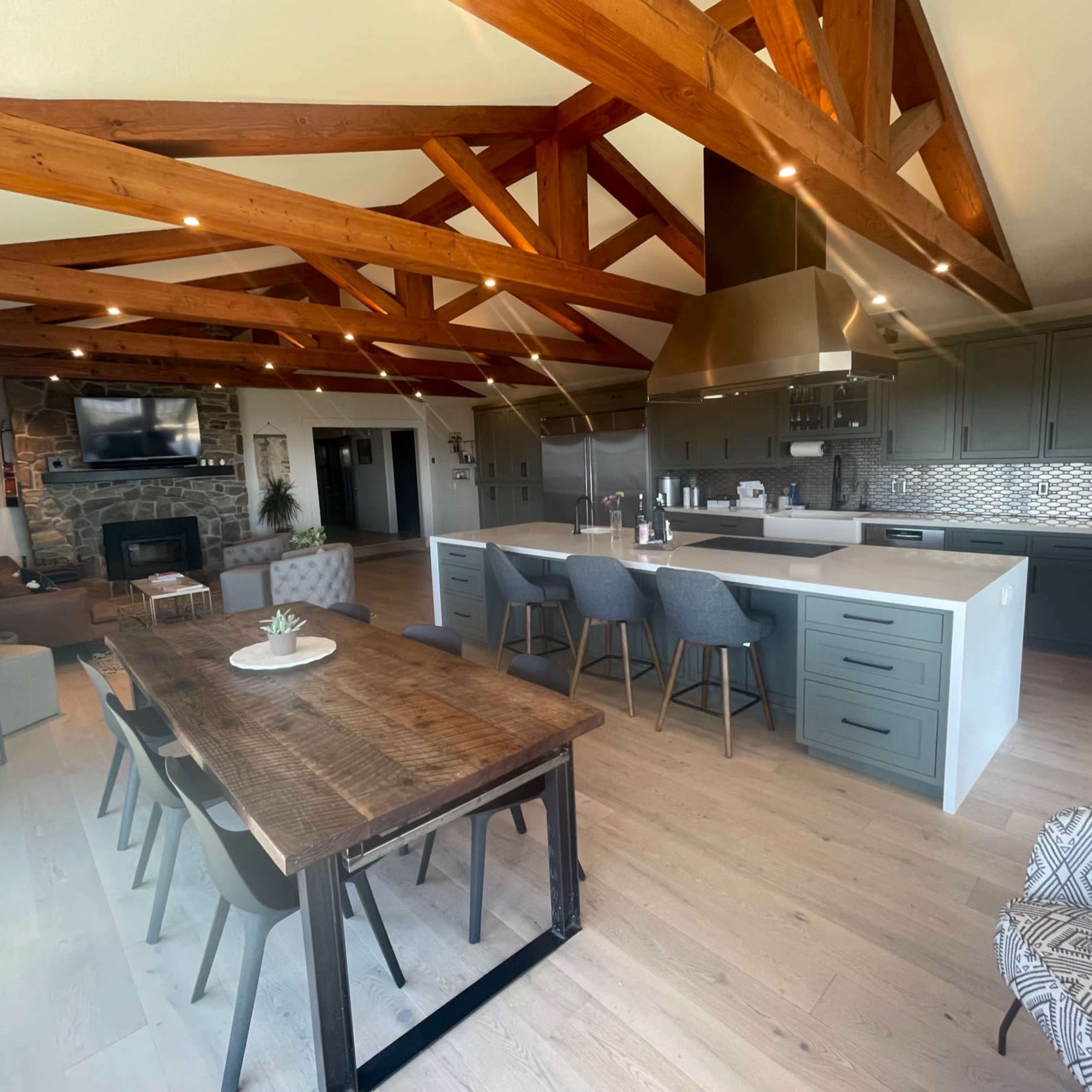 A spacious modern kitchen and dining area featuring wooden beams, a large island with seating, and a rustic dining table.
